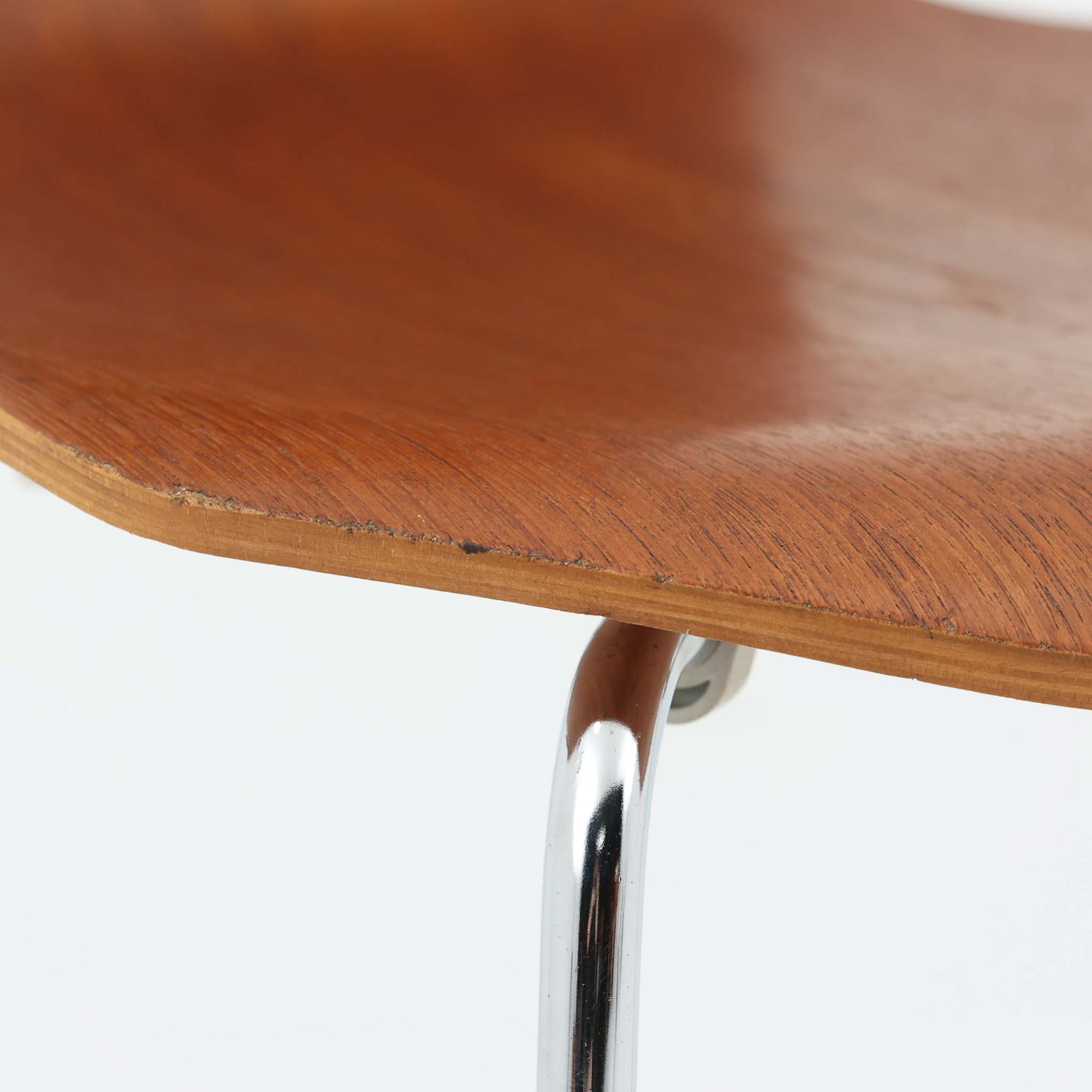 アルネ・ヤコブセンがデザインし、Fritz Hansenが製造した「T Chair」です。チーク材の成形合板による背座一体型のシェルは、背面上部を左右に広げた特徴的なシルエットと、身体に沿う緩やかな曲面が魅力。細身の金属脚との組み合わせが軽快で、ダイニングはもちろん、書斎や玄関のアクセントチェアにもおすすめです。美しい木目と時を重ねた風合い、合理的な構造に宿る北欧ビンテージらしい存在感を楽しめます。