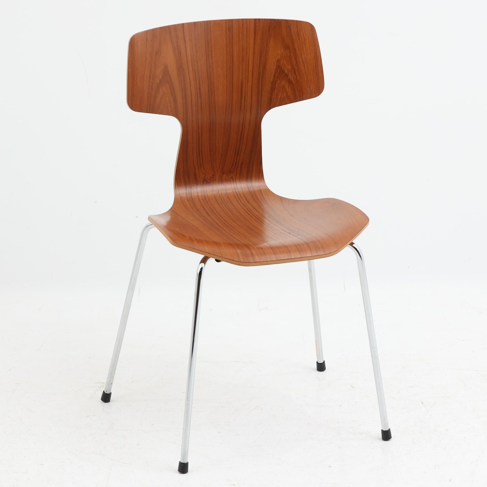 アルネ・ヤコブセンがデザインし、Fritz Hansenが製造した「T Chair」です。チーク材の成形合板による背座一体型のシェルは、背面上部を左右に広げた特徴的なシルエットと、身体に沿う緩やかな曲面が魅力。細身の金属脚との組み合わせが軽快で、ダイニングはもちろん、書斎や玄関のアクセントチェアにもおすすめです。美しい木目と時を重ねた風合い、合理的な構造に宿る北欧ビンテージらしい存在感を楽しめます。