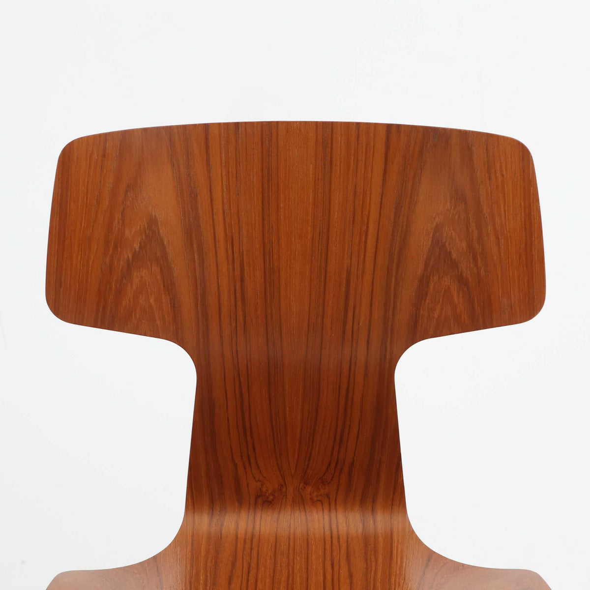アルネ・ヤコブセンがデザインし、Fritz Hansenが製造した「T Chair」です。チーク材の成形合板による背座一体型のシェルは、背面上部を左右に広げた特徴的なシルエットと、身体に沿う緩やかな曲面が魅力。細身の金属脚との組み合わせが軽快で、ダイニングはもちろん、書斎や玄関のアクセントチェアにもおすすめです。美しい木目と時を重ねた風合い、合理的な構造に宿る北欧ビンテージらしい存在感を楽しめます。