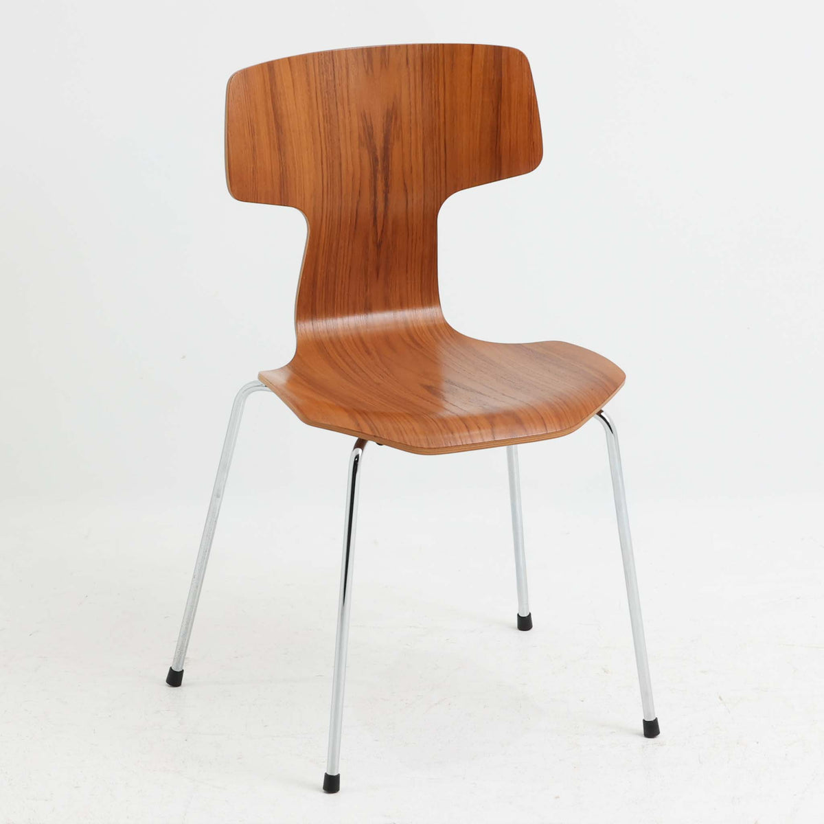アルネ・ヤコブセンがデザインし、Fritz Hansenが製造した「T Chair」です。チーク材の成形合板による背座一体型のシェルは、背面上部を左右に広げた特徴的なシルエットと、身体に沿う緩やかな曲面が魅力。細身の金属脚との組み合わせが軽快で、ダイニングはもちろん、書斎や玄関のアクセントチェアにもおすすめです。美しい木目と時を重ねた風合い、合理的な構造に宿る北欧ビンテージらしい存在感を楽しめます。