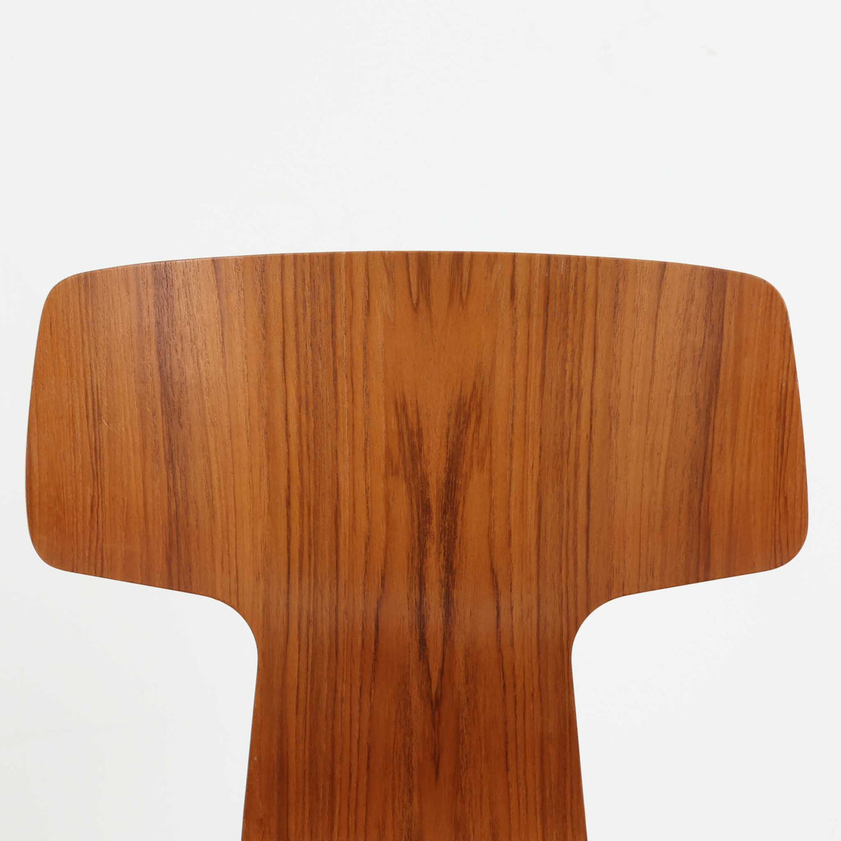 アルネ・ヤコブセンがデザインし、Fritz Hansenが製造した「T Chair」です。チーク材の成形合板による背座一体型のシェルは、背面上部を左右に広げた特徴的なシルエットと、身体に沿う緩やかな曲面が魅力。細身の金属脚との組み合わせが軽快で、ダイニングはもちろん、書斎や玄関のアクセントチェアにもおすすめです。美しい木目と時を重ねた風合い、合理的な構造に宿る北欧ビンテージらしい存在感を楽しめます。