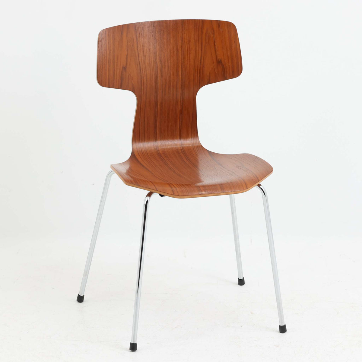 アルネ・ヤコブセンがデザインし、Fritz Hansenが製造した「T Chair」です。チーク材の成形合板による背座一体型のシェルは、背面上部を左右に広げた特徴的なシルエットと、身体に沿う緩やかな曲面が魅力。細身の金属脚との組み合わせが軽快で、ダイニングはもちろん、書斎や玄関のアクセントチェアにもおすすめです。美しい木目と時を重ねた風合い、合理的な構造に宿る北欧ビンテージらしい存在感を楽しめます。