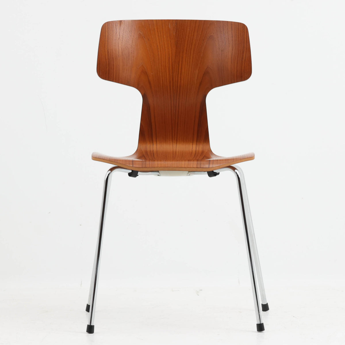 アルネ・ヤコブセンがデザインし、Fritz Hansenが製造した「T Chair」です。チーク材の成形合板による背座一体型のシェルは、背面上部を左右に広げた特徴的なシルエットと、身体に沿う緩やかな曲面が魅力。細身の金属脚との組み合わせが軽快で、ダイニングはもちろん、書斎や玄関のアクセントチェアにもおすすめです。美しい木目と時を重ねた風合い、合理的な構造に宿る北欧ビンテージらしい存在感を楽しめます。
