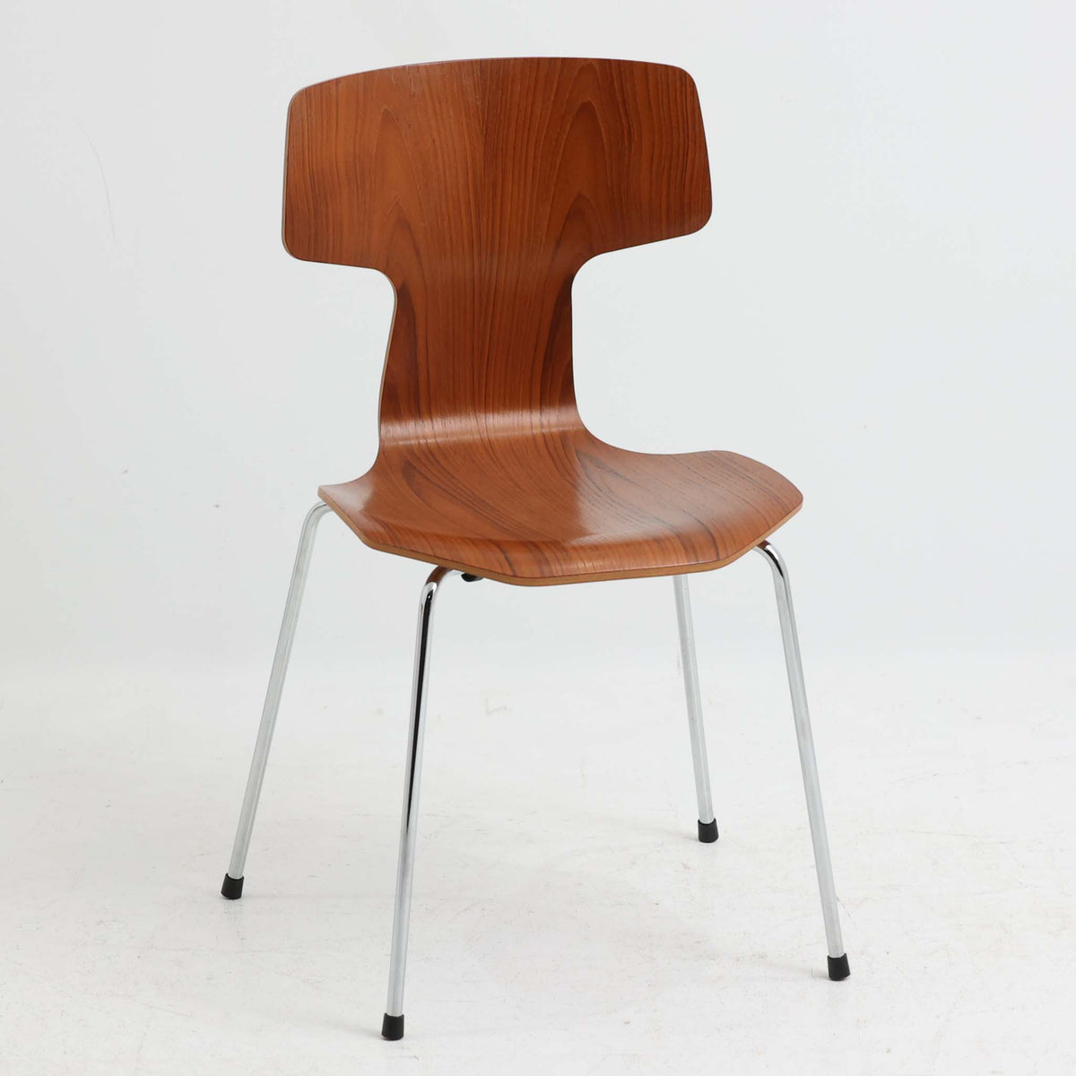 アルネ・ヤコブセンがデザインし、Fritz Hansenが製造した「T Chair」です。チーク材の成形合板による背座一体型のシェルは、背面上部を左右に広げた特徴的なシルエットと、身体に沿う緩やかな曲面が魅力。細身の金属脚との組み合わせが軽快で、ダイニングはもちろん、書斎や玄関のアクセントチェアにもおすすめです。美しい木目と時を重ねた風合い、合理的な構造に宿る北欧ビンテージらしい存在感を楽しめます。