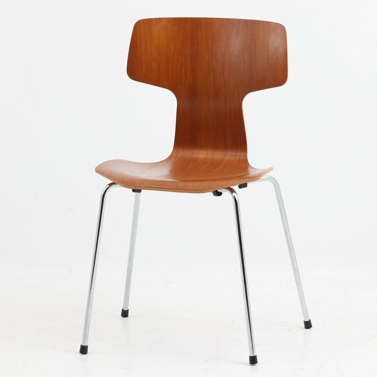アルネ・ヤコブセンがデザインし、Fritz Hansenが製造した「T Chair」です。チーク材の成形合板による背座一体型のシェルは、背面上部を左右に広げた特徴的なシルエットと、身体に沿う緩やかな曲面が魅力。細身の金属脚との組み合わせが軽快で、ダイニングはもちろん、書斎や玄関のアクセントチェアにもおすすめです。美しい木目と時を重ねた風合い、合理的な構造に宿る北欧ビンテージらしい存在感を楽しめます。