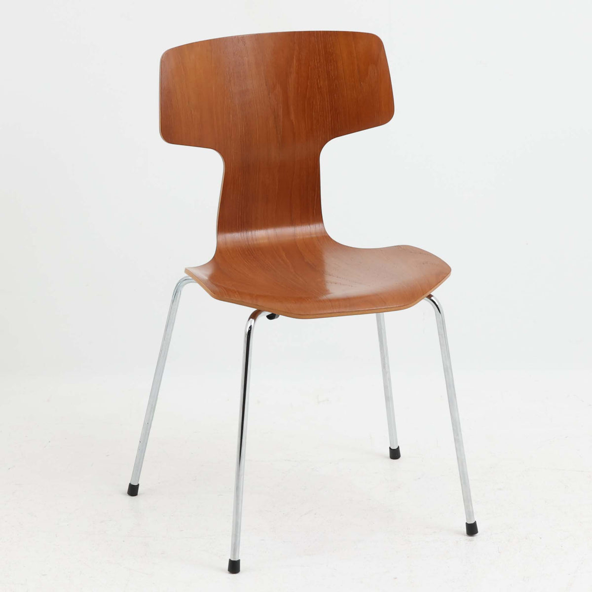 アルネ・ヤコブセンがデザインし、Fritz Hansenが製造した「T Chair」です。チーク材の成形合板による背座一体型のシェルは、背面上部を左右に広げた特徴的なシルエットと、身体に沿う緩やかな曲面が魅力。細身の金属脚との組み合わせが軽快で、ダイニングはもちろん、書斎や玄関のアクセントチェアにもおすすめです。美しい木目と時を重ねた風合い、合理的な構造に宿る北欧ビンテージらしい存在感を楽しめます。