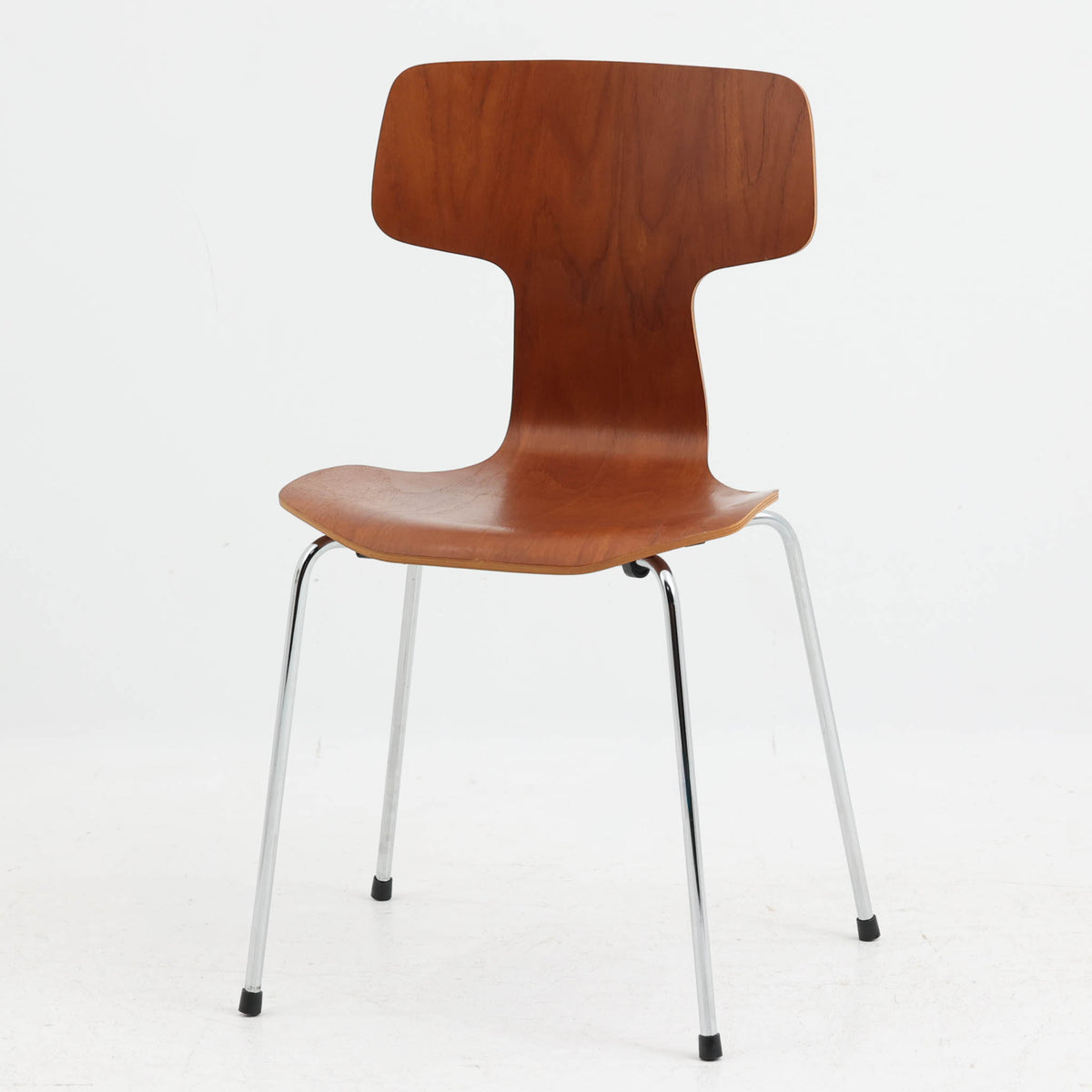 アルネ・ヤコブセンがデザインし、Fritz Hansenが製造した「T Chair」です。チーク材の成形合板による背座一体型のシェルは、背面上部を左右に広げた特徴的なシルエットと、身体に沿う緩やかな曲面が魅力。細身の金属脚との組み合わせが軽快で、ダイニングはもちろん、書斎や玄関のアクセントチェアにもおすすめです。美しい木目と時を重ねた風合い、合理的な構造に宿る北欧ビンテージらしい存在感を楽しめます。