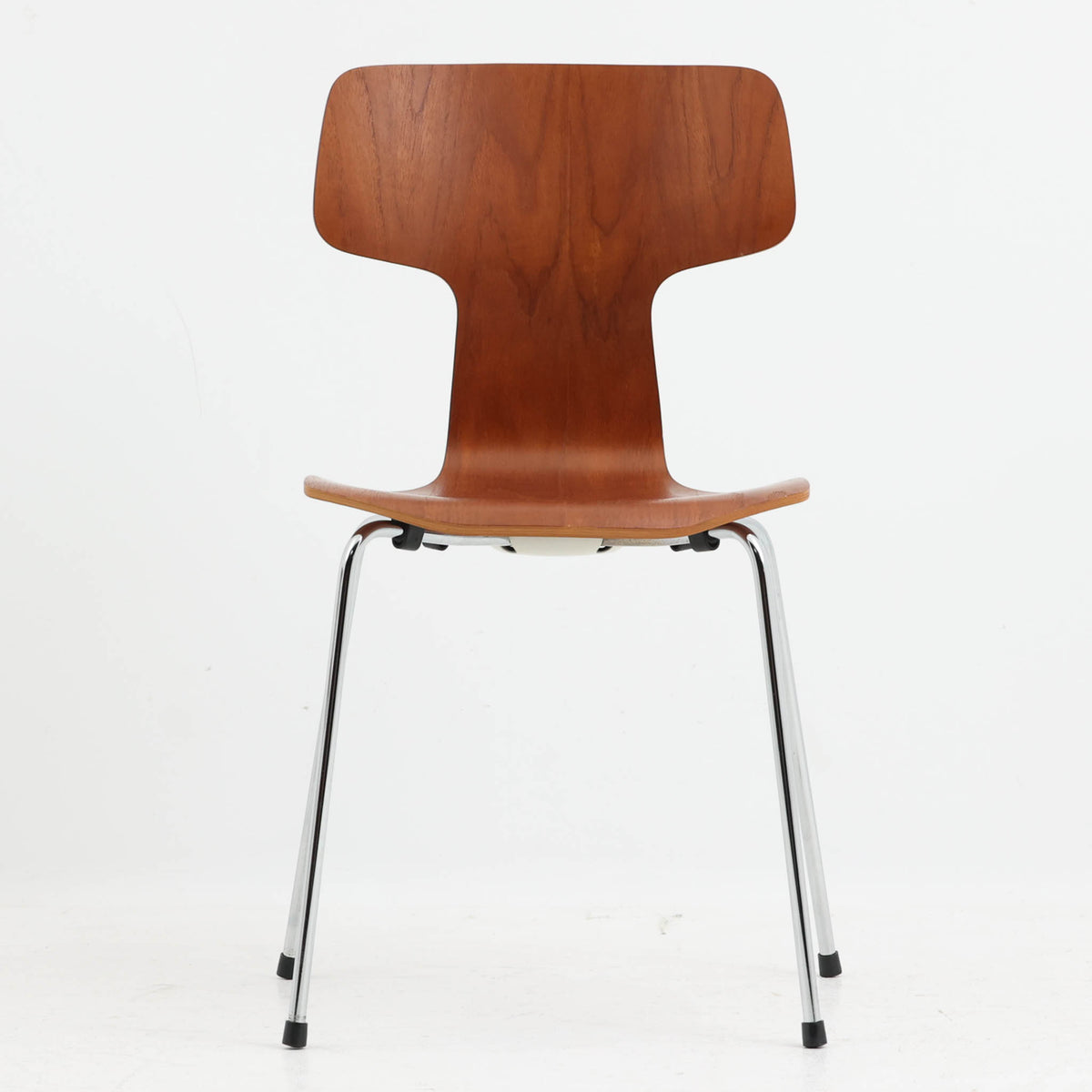 アルネ・ヤコブセンがデザインし、Fritz Hansenが製造した「T Chair」です。チーク材の成形合板による背座一体型のシェルは、背面上部を左右に広げた特徴的なシルエットと、身体に沿う緩やかな曲面が魅力。細身の金属脚との組み合わせが軽快で、ダイニングはもちろん、書斎や玄関のアクセントチェアにもおすすめです。美しい木目と時を重ねた風合い、合理的な構造に宿る北欧ビンテージらしい存在感を楽しめます。