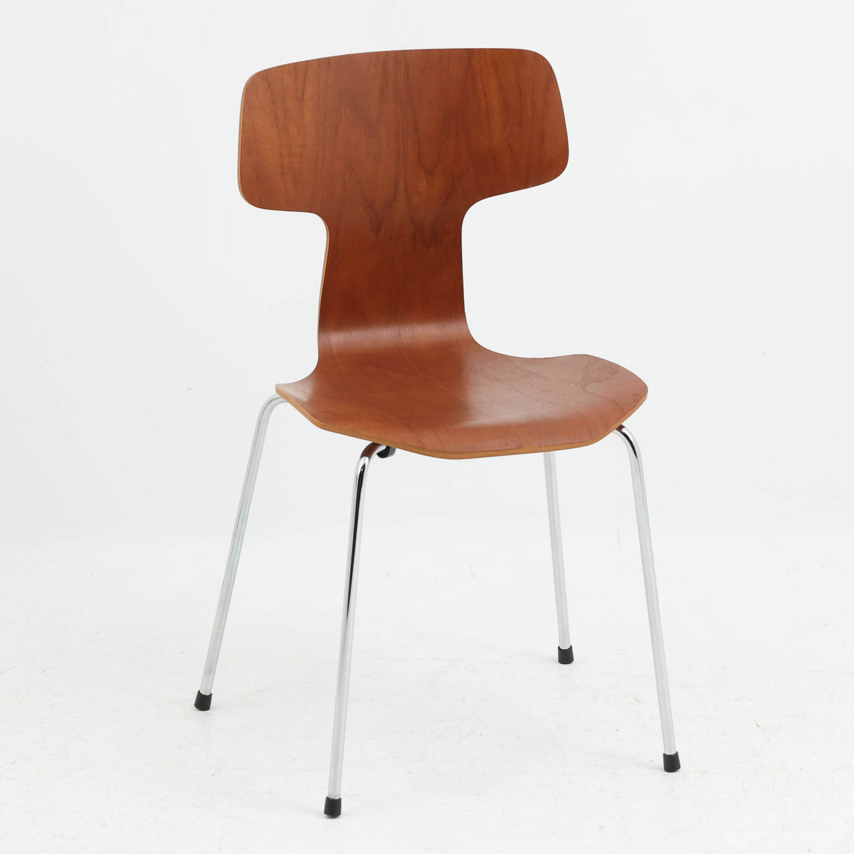 アルネ・ヤコブセンがデザインし、Fritz Hansenが製造した「T Chair」です。チーク材の成形合板による背座一体型のシェルは、背面上部を左右に広げた特徴的なシルエットと、身体に沿う緩やかな曲面が魅力。細身の金属脚との組み合わせが軽快で、ダイニングはもちろん、書斎や玄関のアクセントチェアにもおすすめです。美しい木目と時を重ねた風合い、合理的な構造に宿る北欧ビンテージらしい存在感を楽しめます。