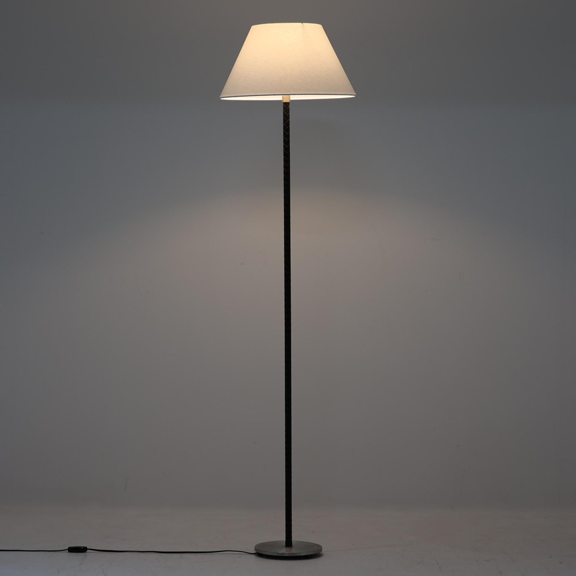 Jo Hammerborgがデザインを手がけ、Fog & Morup社より発表された「Flet」フロアランプは、スチール支柱に丁寧に編み込まれたブラックレザーと、上品なリネンシェードのコントラストが美しい北欧ビンテージ照明です。高さ155cmとすっきりとした佇まいで、空間に程よい存在感をもたらします。経年によるレザーの風合いやシェード越しの柔らかな光が、空間に落ち着いた雰囲気と温もりを加えてくれる一台です。