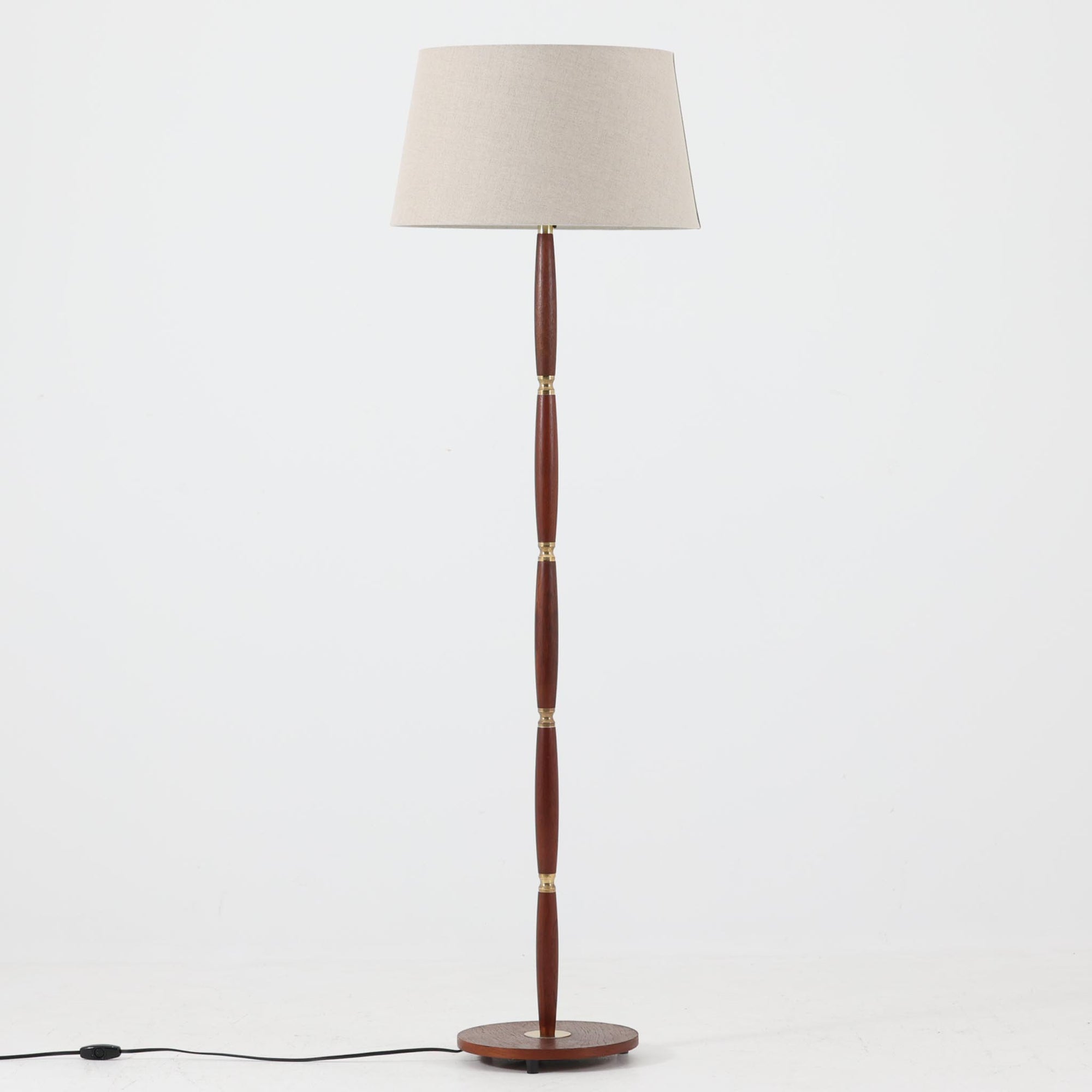 流れるような曲線を描くチーク材の支柱と、節目ごとに配された真鍮パーツが上品なアクセントとなったデンマーク製のビンテージフロアランプです。高さ139cmと程よいサイズ感で、リネンシェードを通して柔らかく広がる光が、読書灯や間接照明としての使用に最適です。木部には温かみある風合いがあり、真鍮の経年変化とも相まって、シンプルながらも重厚感と気品を感じさせる一台です。