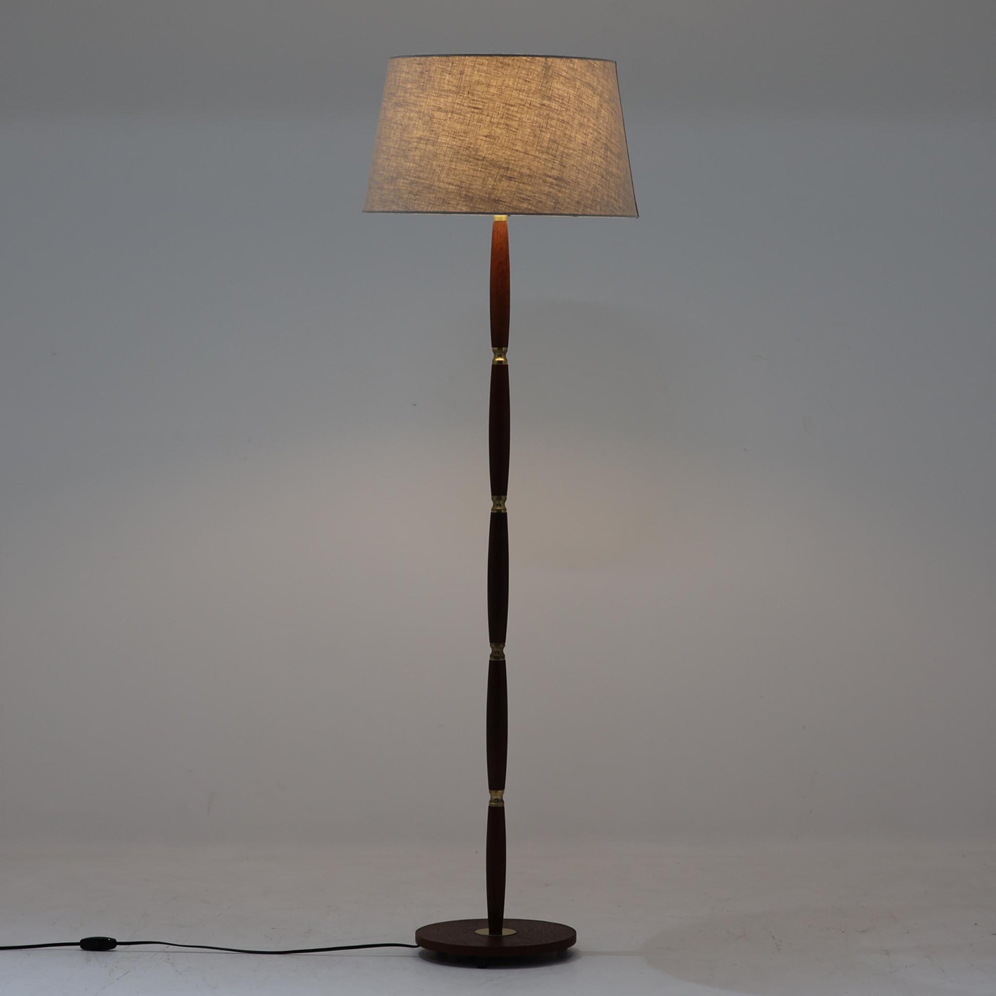 流れるような曲線を描くチーク材の支柱と、節目ごとに配された真鍮パーツが上品なアクセントとなったデンマーク製のビンテージフロアランプです。高さ139cmと程よいサイズ感で、リネンシェードを通して柔らかく広がる光が、読書灯や間接照明としての使用に最適です。木部には温かみある風合いがあり、真鍮の経年変化とも相まって、シンプルながらも重厚感と気品を感じさせる一台です。