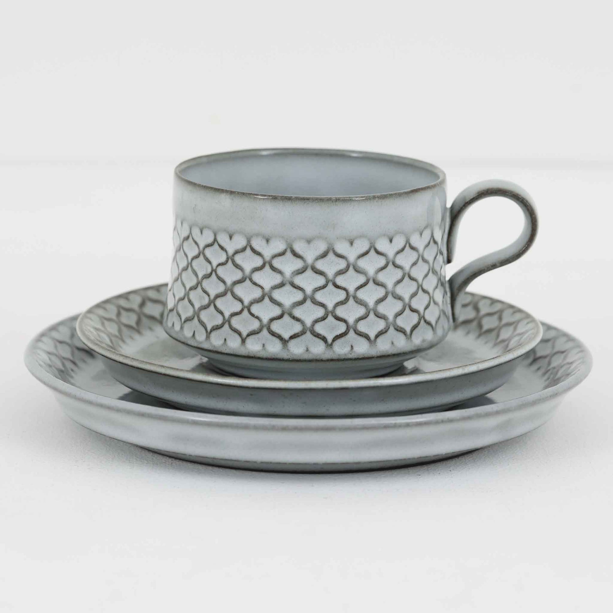 デンマークを代表するデザイナー、イェンス・H・クイストゴーによる「Cordial（コーディアル）」シリーズのヴィンテージ・トリオセット（ティーカップ、ソーサー、プレート）です。1960年代にKronjydenから制作が始まったシリーズは、その後Nissen、Bing&Grondahlと引き継がれ長く愛されたシリーズとなりました。淡いグレーのストーンウェアにハートを連想させる繊細な型押し模様が施されており、デンマークではスウェーデンやフィンランドの陶器メーカーと並んで今でも非常に人気のある商品となります。