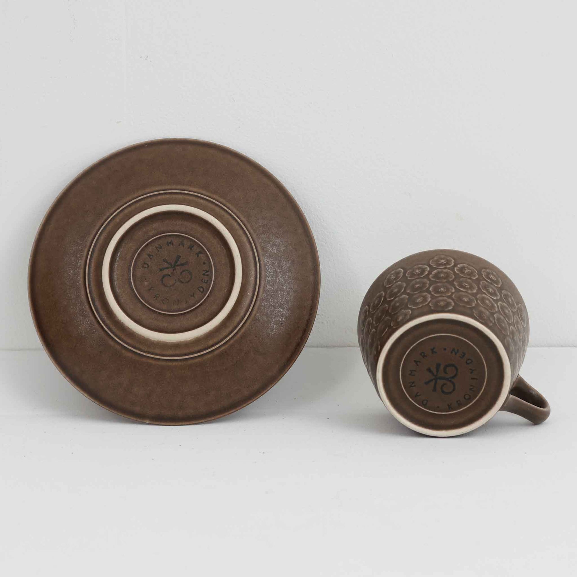 デンマークを代表するデザイナー、イェンス・H・クイストゴーによる「Azur（アズール）」シリーズのヴィンテージカッププ&amp;ソーサーです。1960年代にKronjydenから制作が始まったシリーズは、その後Nissen、Bing&amp;Grondahlと引き継がれ長く愛されたシリーズとなりました。落ち着いたブラウンとプラム色の繊細なフラワーレリーフが施されたストーンウェアは、自然の美しさを食卓にそっと運びます。特にAzurシリーズはヴィンテージ市場でも流通量が極めて少なく高価な逸品となります。