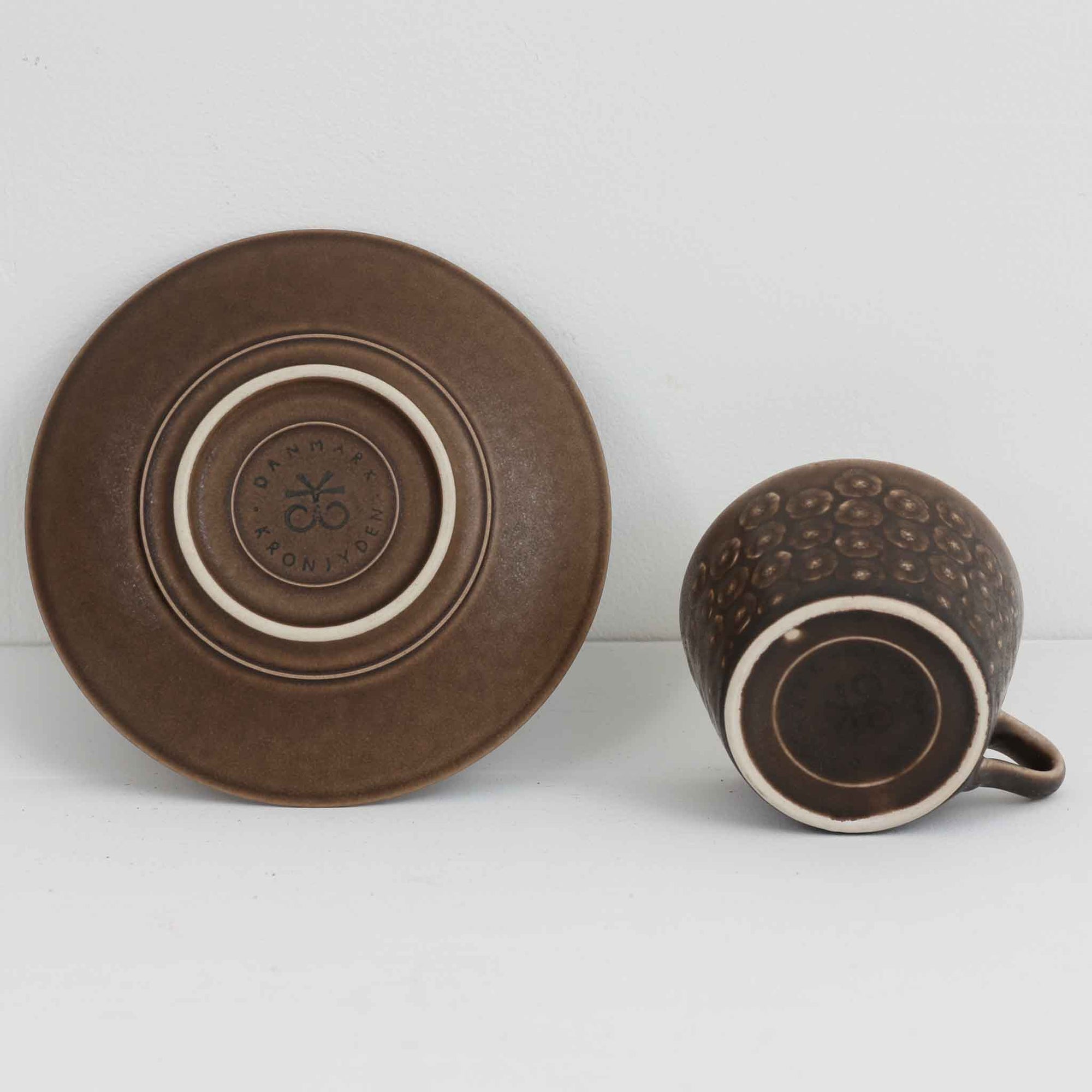デンマークを代表するデザイナー、イェンス・H・クイストゴーによる「Azur（アズール）」シリーズのヴィンテージカッププ&amp;ソーサーです。1960年代にKronjydenから制作が始まったシリーズは、その後Nissen、Bing&amp;Grondahlと引き継がれ長く愛されたシリーズとなりました。落ち着いたブラウンとプラム色の繊細なフラワーレリーフが施されたストーンウェアは、自然の美しさを食卓にそっと運びます。特にAzurシリーズはヴィンテージ市場でも流通量が極めて少なく高価な逸品となります。