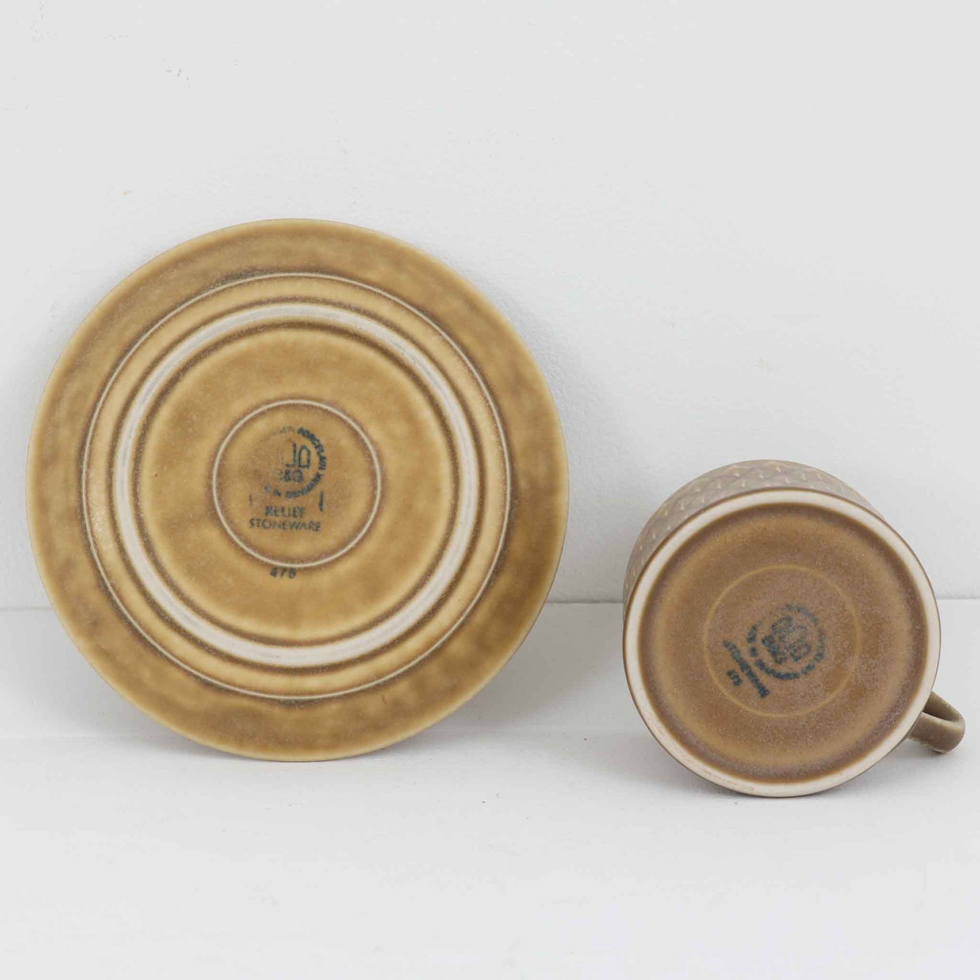 デンマークを代表するデザイナー、イェンス・H・クイストゴーによる「Relief（レリーフ）」シリーズのヴィンテージカップ&amp;ソーサーです。マットなベージュ釉薬に丹念に浮かび上がる葉や木々の〈レリーフ〉装飾が印象的です。素朴で温もりある厚みのあるフォルムは、北欧の静かな森の風景を感じさせます。デンマークではスウェーデンやフィンランドの陶器メーカーと並んで今でも非常に人気のある商品となります。