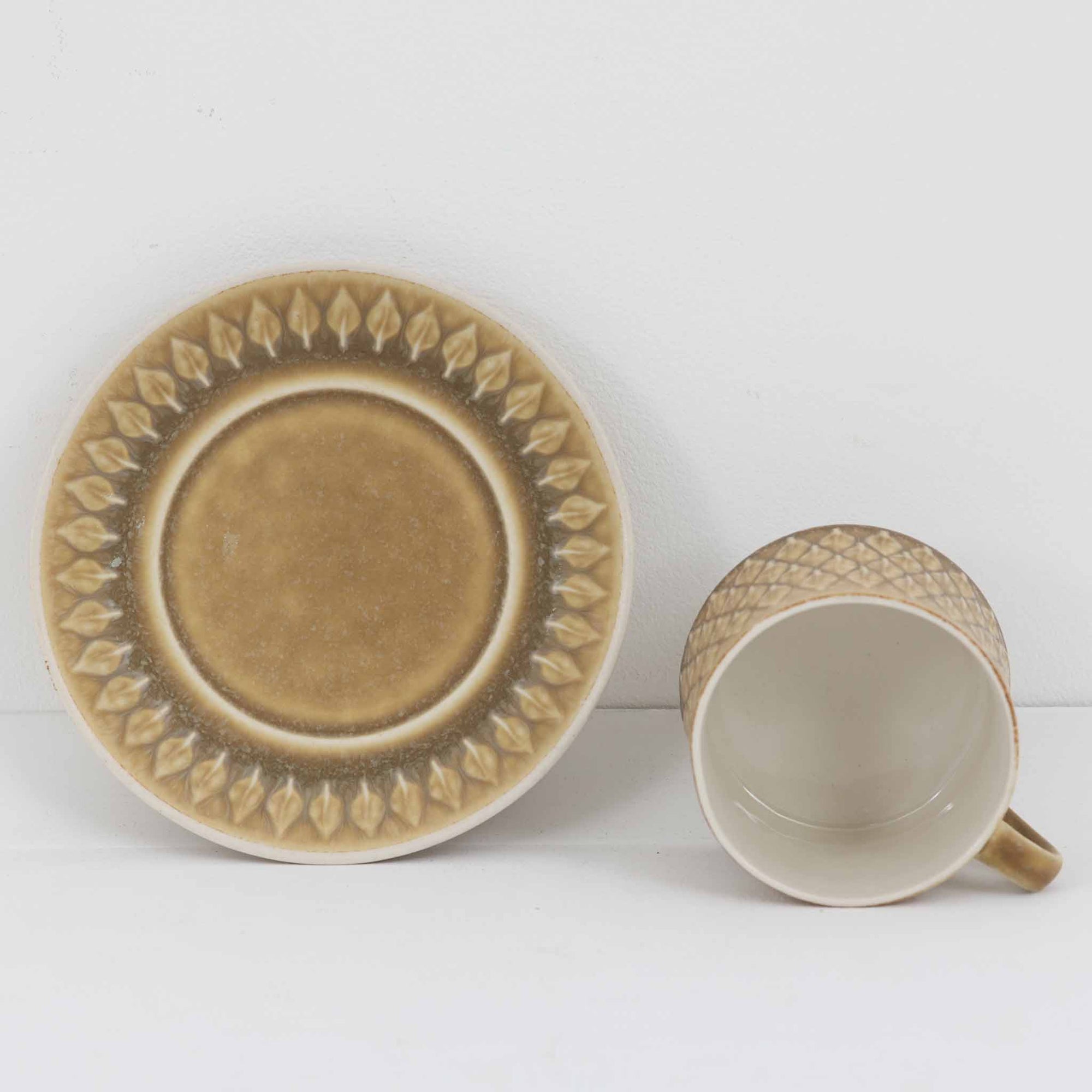 デンマークを代表するデザイナー、イェンス・H・クイストゴーによる「Relief（レリーフ）」シリーズのヴィンテージカップ&ソーサーです。マットなベージュ釉薬に丹念に浮かび上がる葉や木々の〈レリーフ〉装飾が印象的です。素朴で温もりある厚みのあるフォルムは、北欧の静かな森の風景を感じさせます。デンマークではスウェーデンやフィンランドの陶器メーカーと並んで今でも非常に人気のある商品となります。