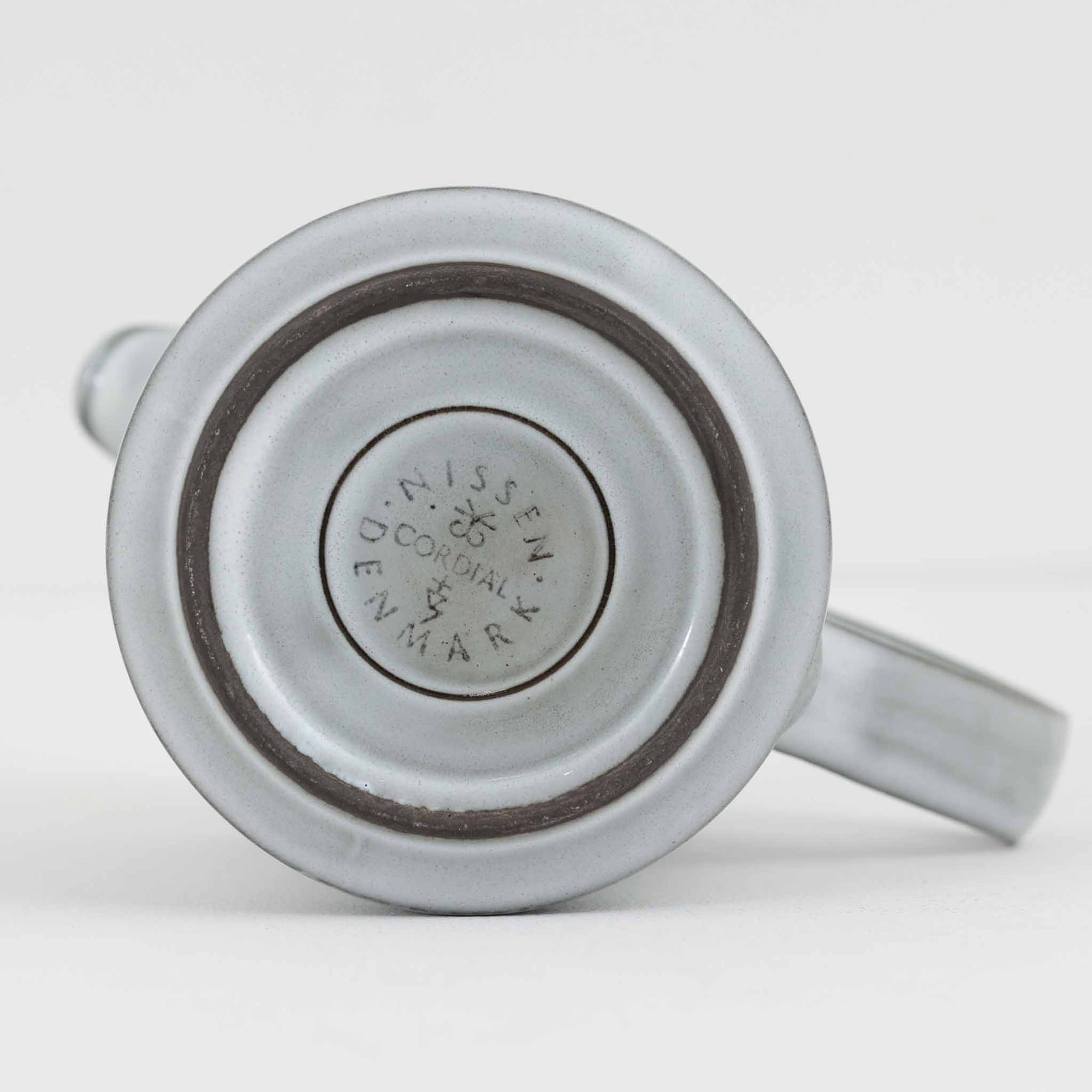 デンマークを代表するデザイナー、イェンス・H・クイストゴーによる「Cordial（コーディアル）」シリーズのヴィンテージ・ミルクジャグ（ピッチャー）です。1960年代にKronjydenから制作が始まったシリーズは、その後Nissen、Bing&amp;Grondahlと引き継がれ長く愛されたシリーズとなりました。淡いグレーのストーンウェアにハートを連想させる繊細な型押し模様が施されており、デンマークではスウェーデンやフィンランドの陶器メーカーと並んで今でも非常に人気のある商品となります。