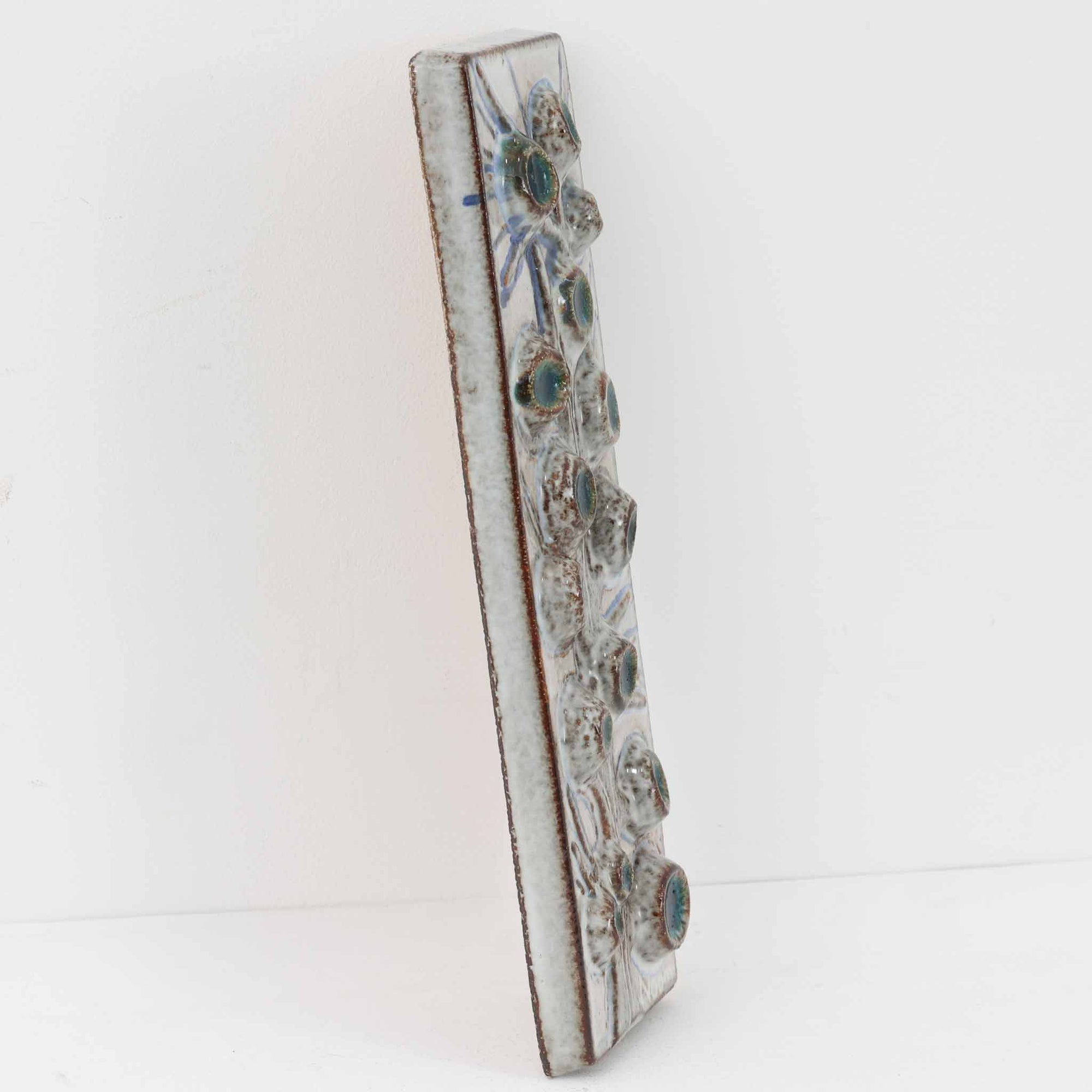 デンマークの名窯Søholm（スーホルム）による、ヴィンテージ陶器の壁掛けプレートです。枝に咲く花々をモチーフとしたレリーフが印象的で、淡く優しい釉薬の色合いと立体的な表現が、北欧らしいあたたかみと静かな存在感を演出します。デザインを手がけたのは、Søholmを代表する女性アーティストの一人、Noomi Backhausen（ノオミ・バッカウセン）。彼女ならではの柔らかい造形と繊細な表現が生きた一枚です。