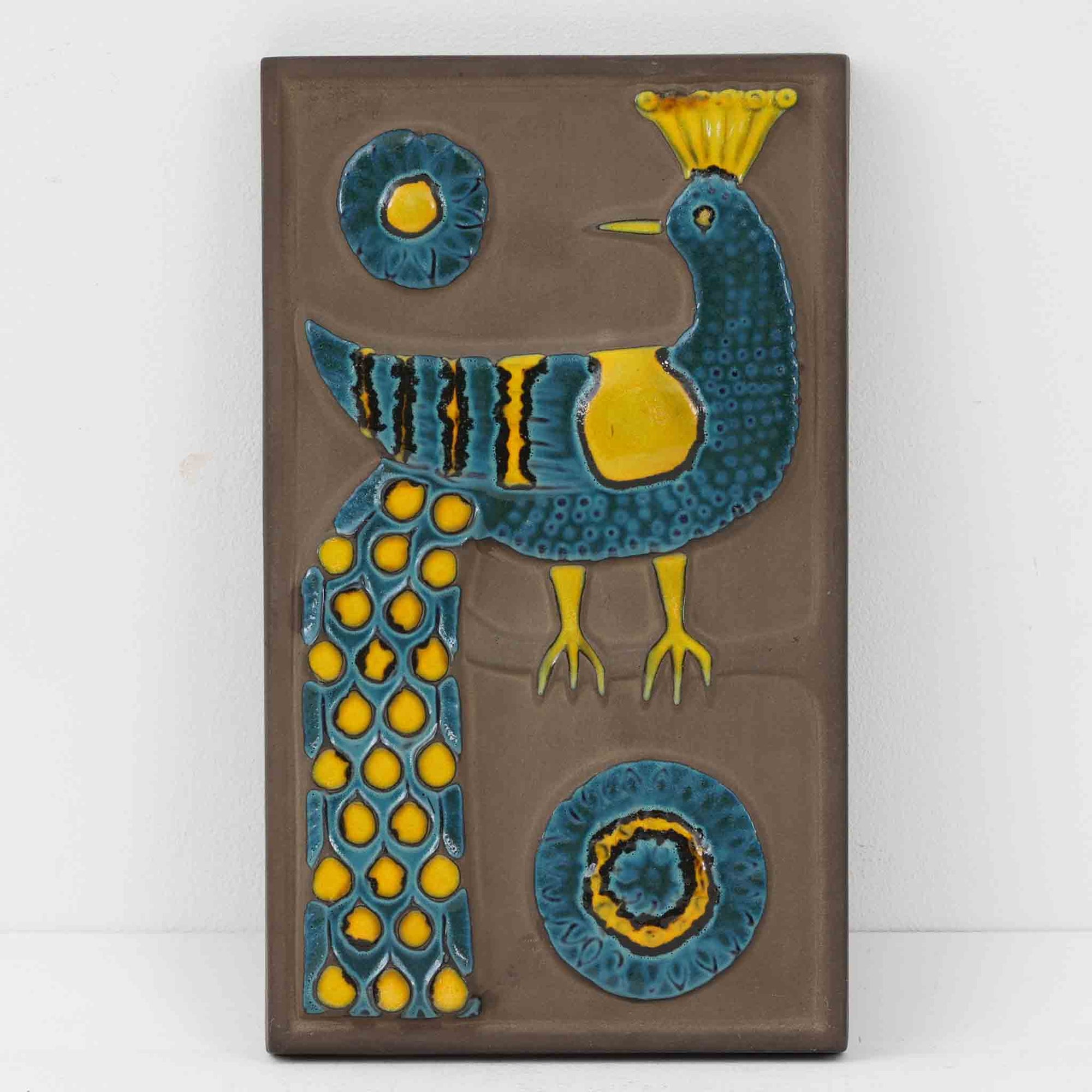 デンマークの老舗陶器メーカー Knabstrup（クナブストルプ）による、ヴィンテージ陶器の壁掛けプレート「Relief pafugl」。ブルーとイエローを基調とした孔雀（または孔雀を思わせる鳥）がレリーフで描かれており、ミッドセンチュリー期の北欧陶器らしい大胆さと繊細さを兼ね備えた一枚です。デザインを手がけたのは、当時 Knabstrup に所属していた陶芸家 Gunter Praschak。有機的なフォルムと鮮やかな色遣い、立体的なレリーフの陰影が、壁に飾ることで空間にアクセントとクラフト感を与えます。