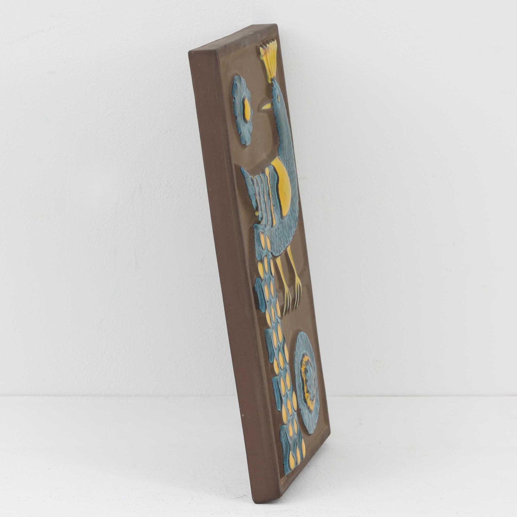 デンマークの老舗陶器メーカー Knabstrup（クナブストルプ）による、ヴィンテージ陶器の壁掛けプレート「Relief pafugl」。ブルーとイエローを基調とした孔雀（または孔雀を思わせる鳥）がレリーフで描かれており、ミッドセンチュリー期の北欧陶器らしい大胆さと繊細さを兼ね備えた一枚です。デザインを手がけたのは、当時 Knabstrup に所属していた陶芸家 Gunter Praschak。有機的なフォルムと鮮やかな色遣い、立体的なレリーフの陰影が、壁に飾ることで空間にアクセントとクラフト感を与えます。