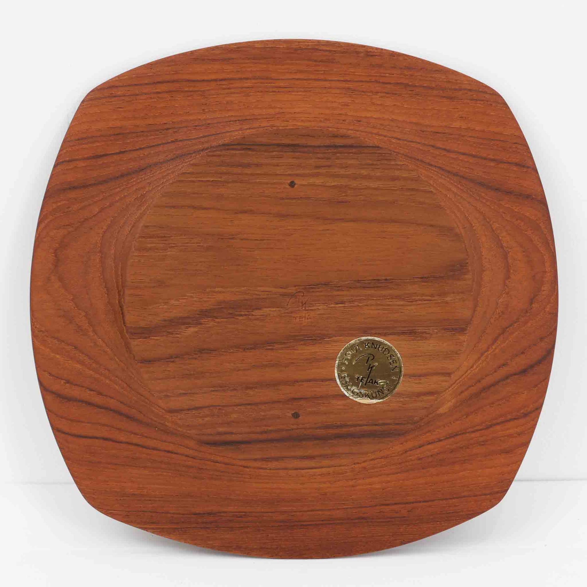 1960年代、デンマーク・モダンの黄金期にポール・クヌーセンが手がけたチーク無垢材のプレートです。「実用工芸」を意味するブランド名の通り、木の質感を活かした滑らかな曲線と、洗練されたミニマルな造形美が魅力。半世紀を経て深く色づいたチーク材は「木の宝石」と称されるほど美しく、食卓に温かな品格を添えます。食器としてはもちろん、インテリアトレイとしても重宝する、一期一会のヴィンテージ名作です。