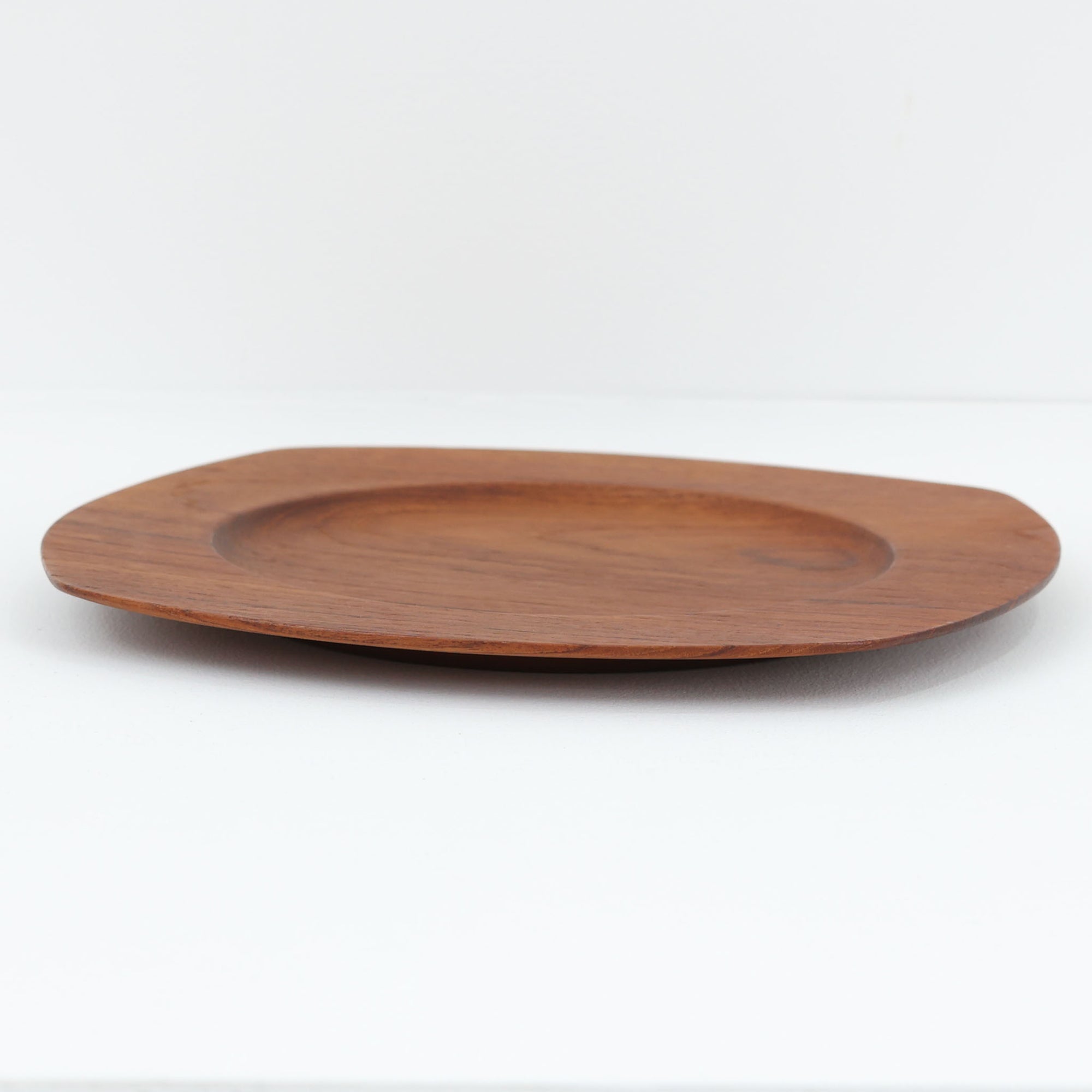 1960年代、デンマーク・モダンの黄金期にポール・クヌーセンが手がけたチーク無垢材のプレートです。「実用工芸」を意味するブランド名の通り、木の質感を活かした滑らかな曲線と、洗練されたミニマルな造形美が魅力。半世紀を経て深く色づいたチーク材は「木の宝石」と称されるほど美しく、食卓に温かな品格を添えます。食器としてはもちろん、インテリアトレイとしても重宝する、一期一会のヴィンテージ名作です。