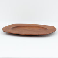 1960年代、デンマーク・モダンの黄金期にポール・クヌーセンが手がけたチーク無垢材のプレートです。「実用工芸」を意味するブランド名の通り、木の質感を活かした滑らかな曲線と、洗練されたミニマルな造形美が魅力。半世紀を経て深く色づいたチーク材は「木の宝石」と称されるほど美しく、食卓に温かな品格を添えます。食器としてはもちろん、インテリアトレイとしても重宝する、一期一会のヴィンテージ名作です。