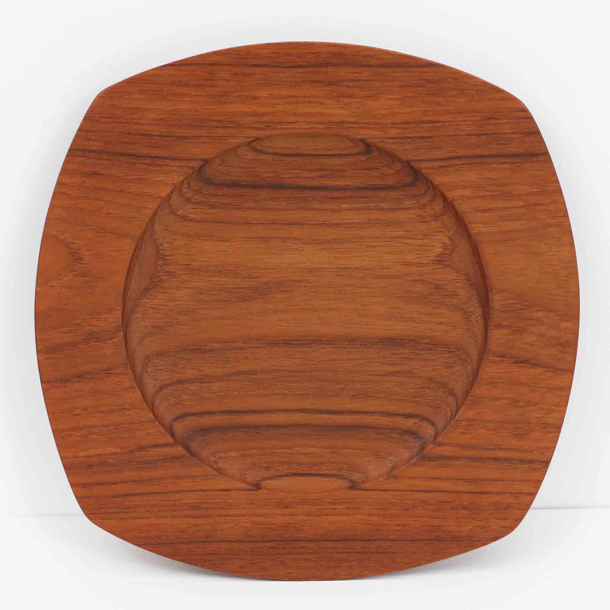 1960年代、デンマーク・モダンの黄金期にポール・クヌーセンが手がけたチーク無垢材のプレートです。「実用工芸」を意味するブランド名の通り、木の質感を活かした滑らかな曲線と、洗練されたミニマルな造形美が魅力。半世紀を経て深く色づいたチーク材は「木の宝石」と称されるほど美しく、食卓に温かな品格を添えます。食器としてはもちろん、インテリアトレイとしても重宝する、一期一会のヴィンテージ名作です。