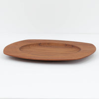 1960年代、デンマーク・モダンの黄金期にポール・クヌーセンが手がけたチーク無垢材のプレートです。「実用工芸」を意味するブランド名の通り、木の質感を活かした滑らかな曲線と、洗練されたミニマルな造形美が魅力。半世紀を経て深く色づいたチーク材は「木の宝石」と称されるほど美しく、食卓に温かな品格を添えます。食器としてはもちろん、インテリアトレイとしても重宝する、一期一会のヴィンテージ名作です。