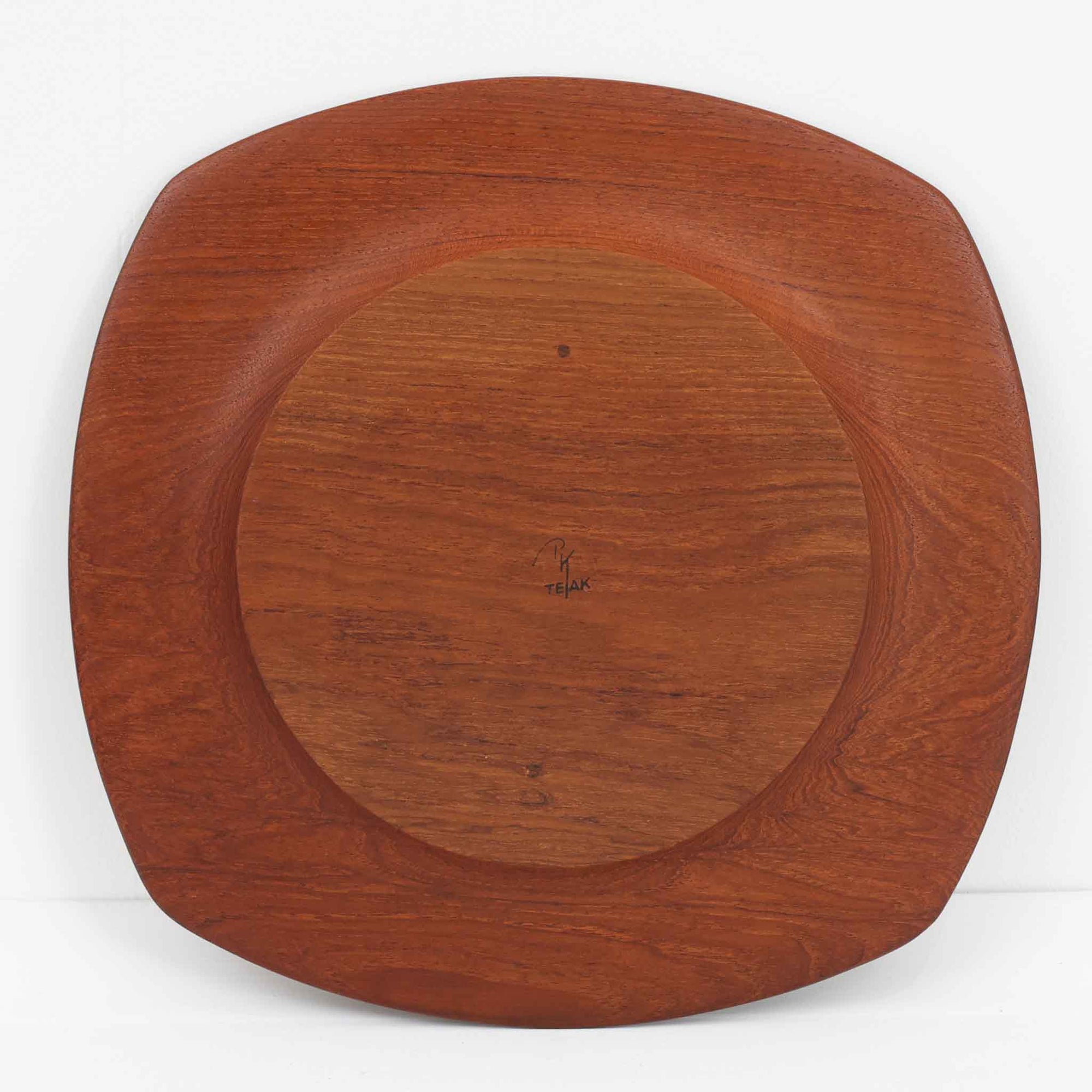 1960年代、デンマーク・モダンの黄金期にポール・クヌーセンが手がけたチーク無垢材のプレートです。「実用工芸」を意味するブランド名の通り、木の質感を活かした滑らかな曲線と、洗練されたミニマルな造形美が魅力。半世紀を経て深く色づいたチーク材は「木の宝石」と称されるほど美しく、食卓に温かな品格を添えます。食器としてはもちろん、インテリアトレイとしても重宝する、一期一会のヴィンテージ名作です。