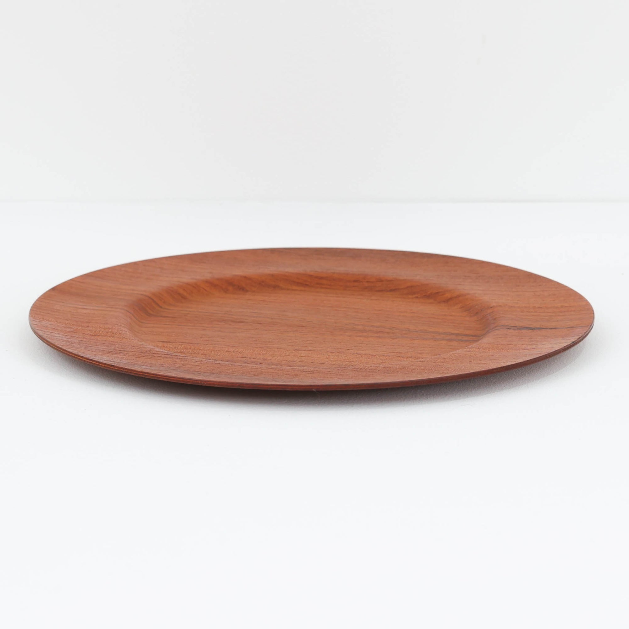 北欧ヴィンテージらしい、あたたかみのある木目が魅力のチーク材プレートです。突板（プライウッド）仕様のため、軽やかで扱いやすく、テーブルの雰囲気を上品にまとめてくれます。メーカー刻印等は見当たらず詳細は不明ですが、形状や素材感から1960年代頃のデンマーク製と思われます。アクセサリートレイや小物置きとしても使いやすい一枚です。