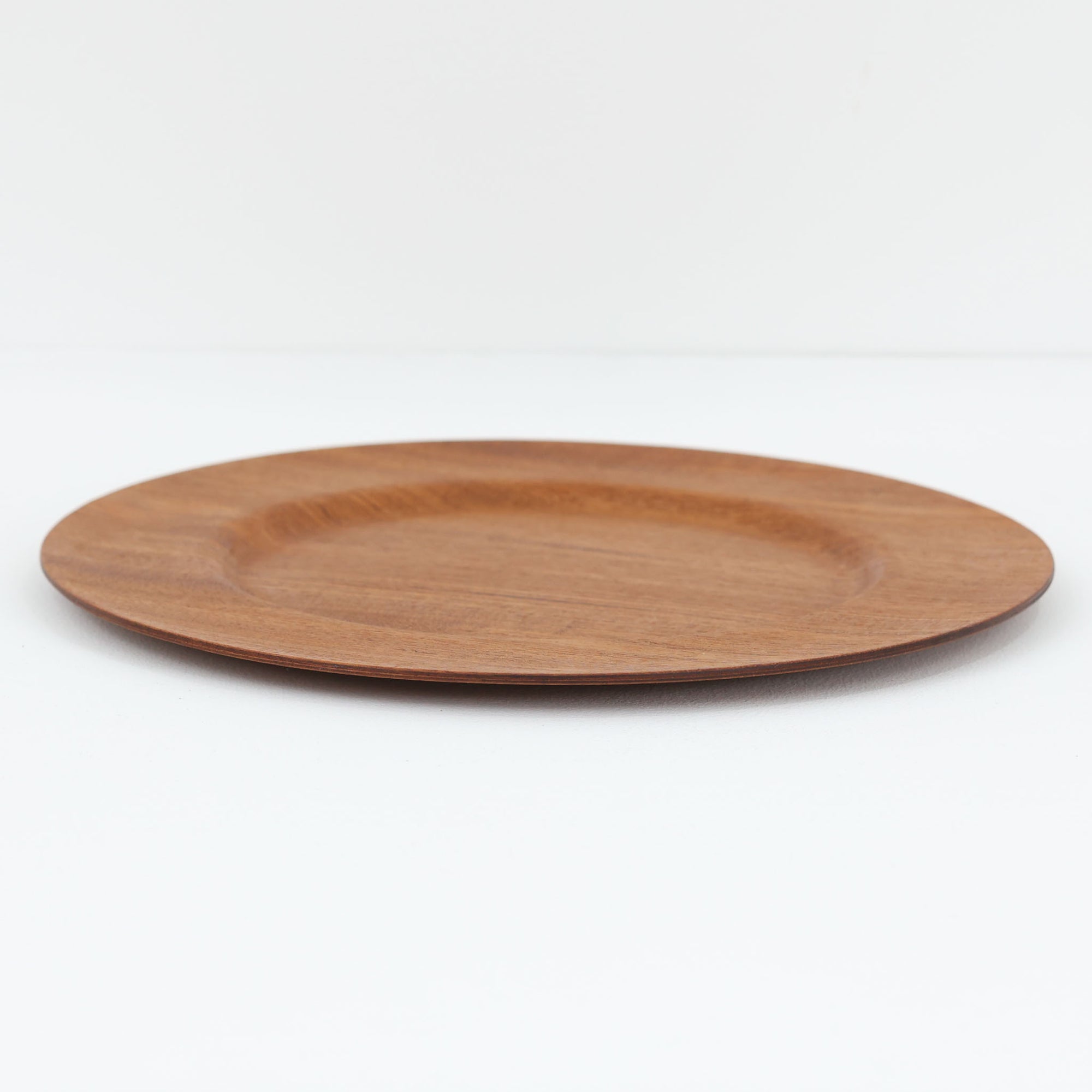 北欧ヴィンテージらしい、あたたかみのある木目が魅力のチーク材プレートです。突板（プライウッド）仕様のため、軽やかで扱いやすく、テーブルの雰囲気を上品にまとめてくれます。メーカー刻印等は見当たらず詳細は不明ですが、形状や素材感から1960年代頃のデンマーク製と思われます。アクセサリートレイや小物置きとしても使いやすい一枚です。