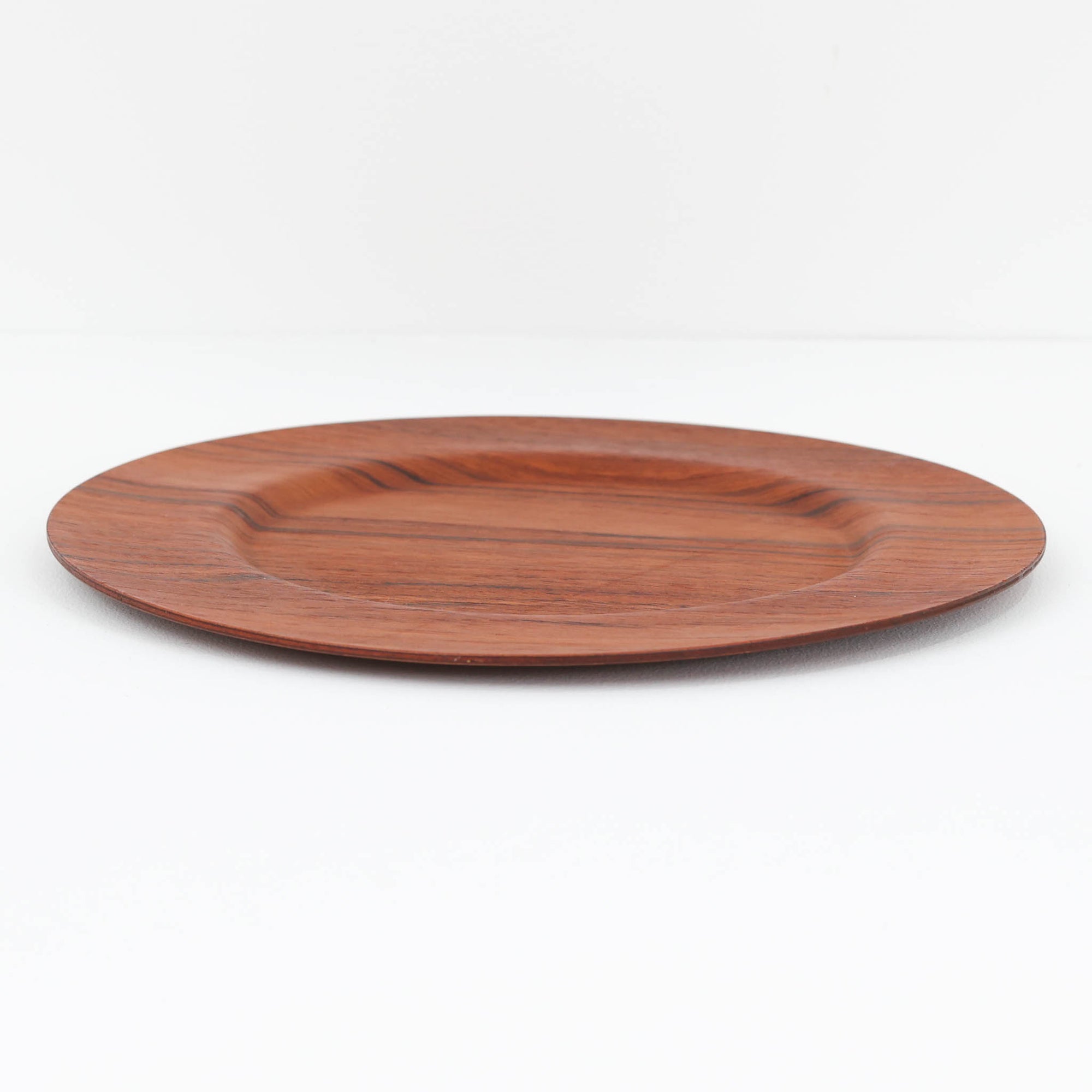 北欧ヴィンテージらしい、あたたかみのある木目が魅力のチーク材プレートです。突板（プライウッド）仕様のため、軽やかで扱いやすく、テーブルの雰囲気を上品にまとめてくれます。メーカー刻印等は見当たらず詳細は不明ですが、形状や素材感から1960年代頃のデンマーク製と思われます。アクセサリートレイや小物置きとしても使いやすい一枚です。