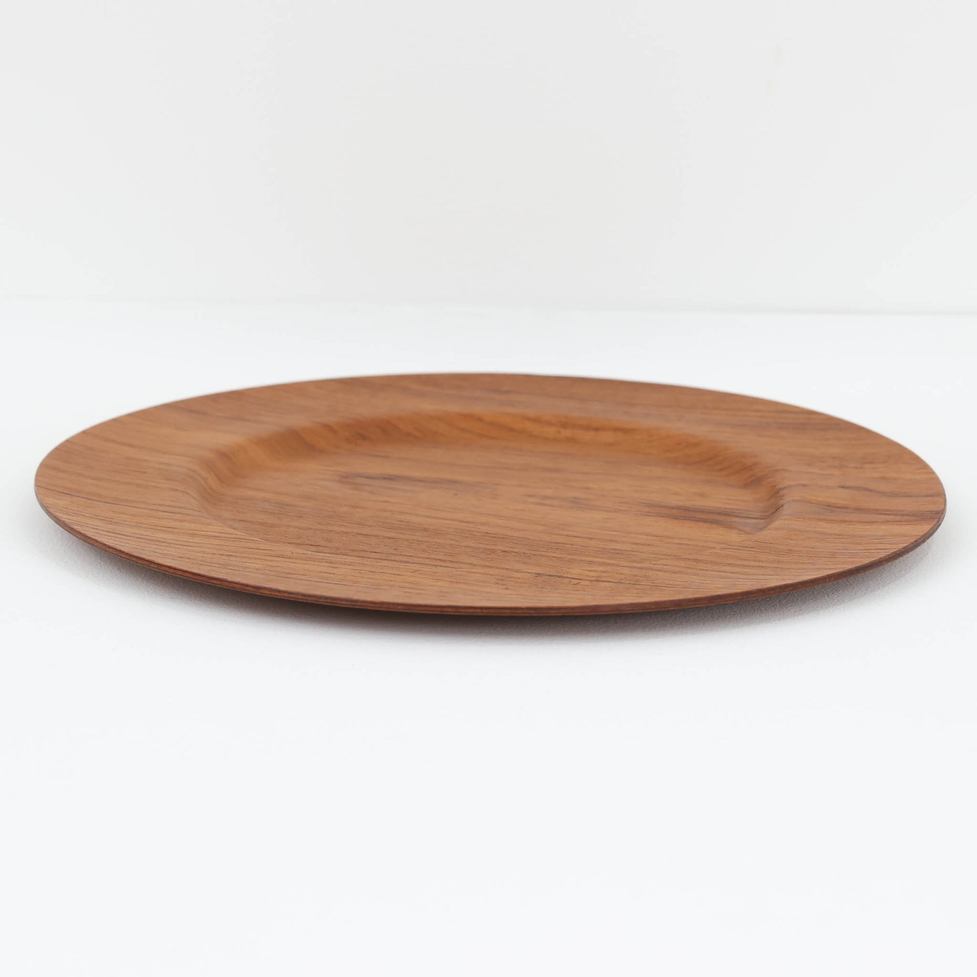 北欧ヴィンテージらしい、あたたかみのある木目が魅力のチーク材プレートです。突板（プライウッド）仕様のため、軽やかで扱いやすく、テーブルの雰囲気を上品にまとめてくれます。メーカー刻印等は見当たらず詳細は不明ですが、形状や素材感から1960年代頃のデンマーク製と思われます。アクセサリートレイや小物置きとしても使いやすい一枚です。