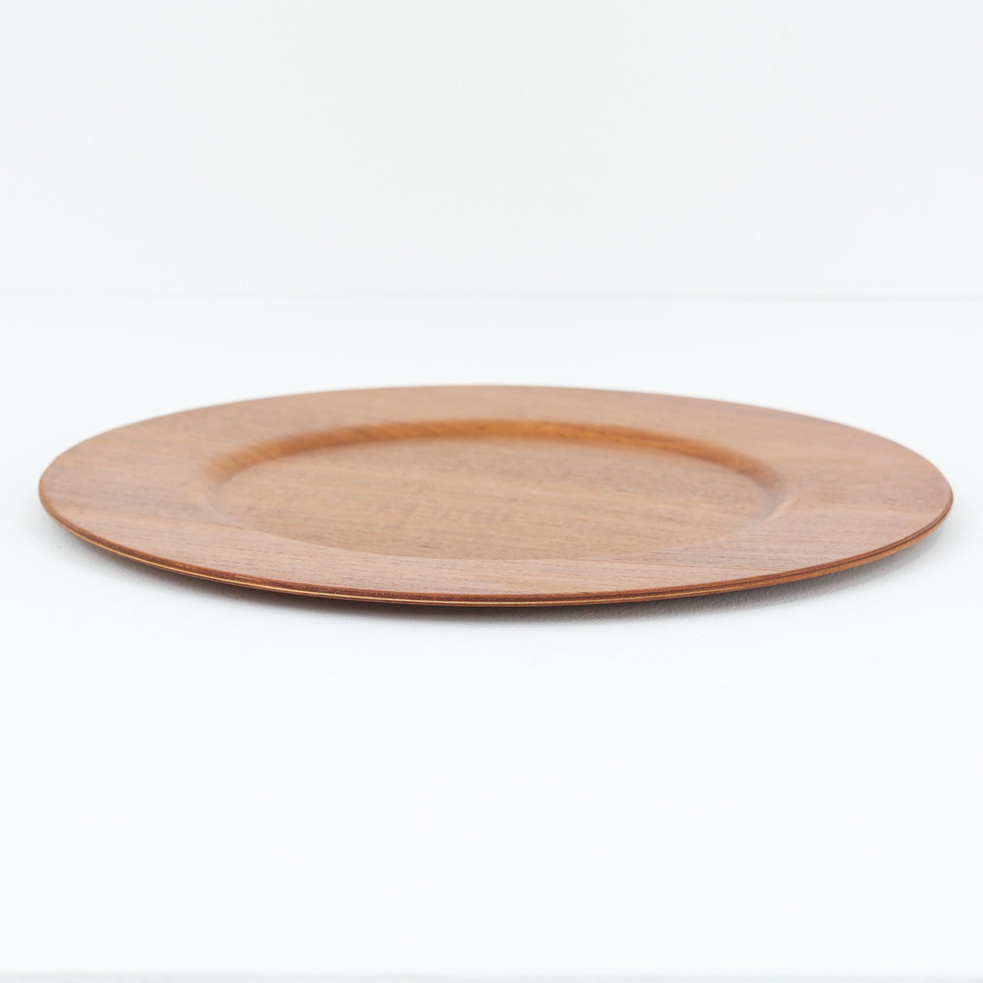 北欧ヴィンテージらしい、あたたかみのある木目が魅力のチーク材プレートです。突板（プライウッド）仕様のため、軽やかで扱いやすく、テーブルの雰囲気を上品にまとめてくれます。メーカー刻印等は見当たらず詳細は不明ですが、形状や素材感から1960年代頃のデンマーク製と思われます。アクセサリートレイや小物置きとしても使いやすい一枚です。