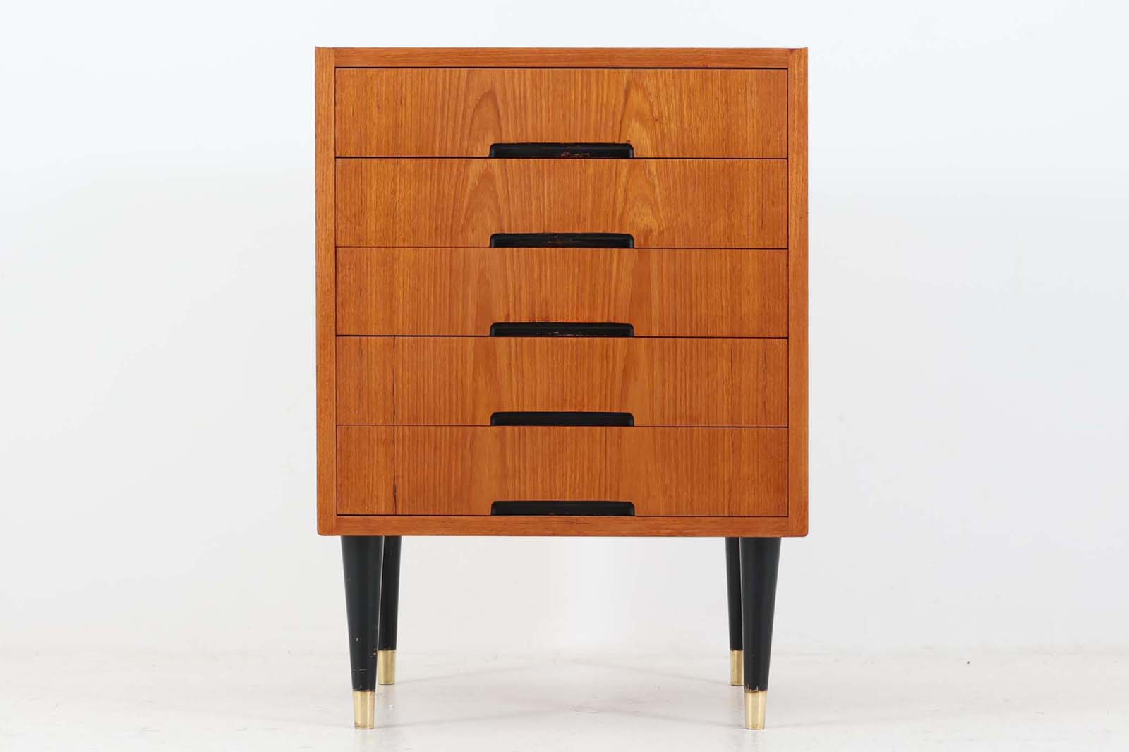 スウェーデンより買い付けた5段チェストです。ブラックペイントと良質なチーク材の組み合わせが素敵です。ゴールド色の脚先がデザインポイントになっています。横から見ると削り出された取手により本体はフラットでスタイリッシュな印象を受けます。天板サイド部は物が落ちにくい様に少しの返しがございます。