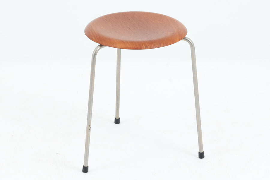 1954年、デンマークのデザイナー、Arne Jacobsen（アルネ・ヤコブセン）によって発表された3本脚のスツール、「DOT（ドット）」。このスツールは、ヤコブセンが手がけた「ルードブレ市庁舎」のロビーで待合席として使用されていました。1970年には4本脚のバージョンも登場しましたが、3本脚のモデルは同年に廃盤となり、現在はビンテージ品のみで入手可能です。オフィスや自宅での日常的な使用はもちろん、予備の椅子としても便利なこのスツールは、シンプルなデザインが魅力です。座面の中央がわずかにくぼんでおり、座った際にフィット感を生み出します。シンプルながらもヤコブセンのこだわりが感じられ、また、単なるスツールとしてだけでなく、ソファの横に置いて本や小物を置くサイドテーブルとしても活用できます。座面裏には薄っすらとFritz Hansen社の刻印がございます。