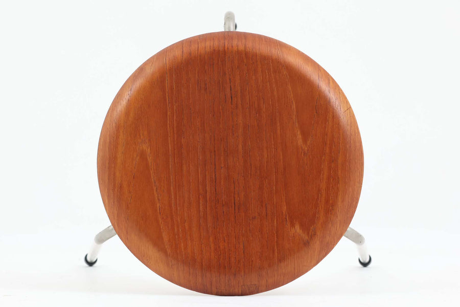 1954年、デンマークのデザイナー、Arne Jacobsen（アルネ・ヤコブセン）によって発表された3本脚のスツール、「DOT（ドット）」。このスツールは、ヤコブセンが手がけた「ルードブレ市庁舎」のロビーで待合席として使用されていました。1970年には4本脚のバージョンも登場しましたが、3本脚のモデルは同年に廃盤となり、現在はビンテージ品のみで入手可能です。オフィスや自宅での日常的な使用はもちろん、予備の椅子としても便利なこのスツールは、シンプルなデザインが魅力です。座面の中央がわずかにくぼんでおり、座った際にフィット感を生み出します。シンプルながらもヤコブセンのこだわりが感じられ、また、単なるスツールとしてだけでなく、ソファの横に置いて本や小物を置くサイドテーブルとしても活用できます。座面裏には薄っすらとFritz Hansen社の刻印がございます。