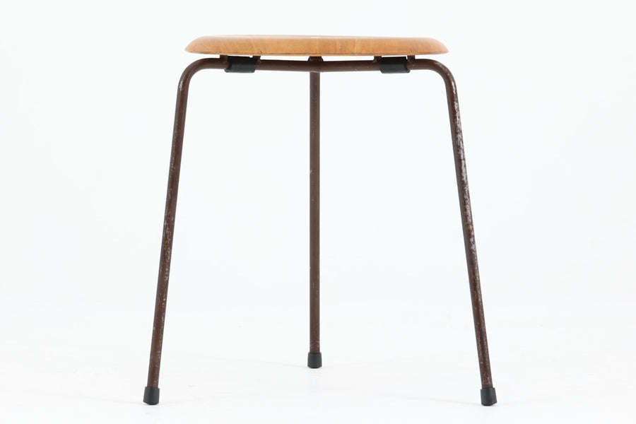 1954年、デンマークのデザイナー、Arne Jacobsen（アルネ・ヤコブセン）によって発表された3本脚のスツール、「DOT（ドット）」。このスツールは、ヤコブセンが手がけた「ルードブレ市庁舎」のロビーで待合席として使用されていました。1970年には4本脚のバージョンも登場しましたが、3本脚のモデルは同年に廃盤となり、現在はビンテージ品のみで入手可能です。オフィスや自宅での日常的な使用はもちろん、予備の椅子としても便利なこのスツールは、シンプルなデザインが魅力です。座面の中央がわずかにくぼんでおり、座った際にフィット感を生み出します。シンプルながらもヤコブセンのこだわりが感じられ、また、単なるスツールとしてだけでなく、ソファの横に置いて本や小物を置くサイドテーブルとしても活用できます。座面裏には薄っすらとFritz Hansen社の刻印がございます。