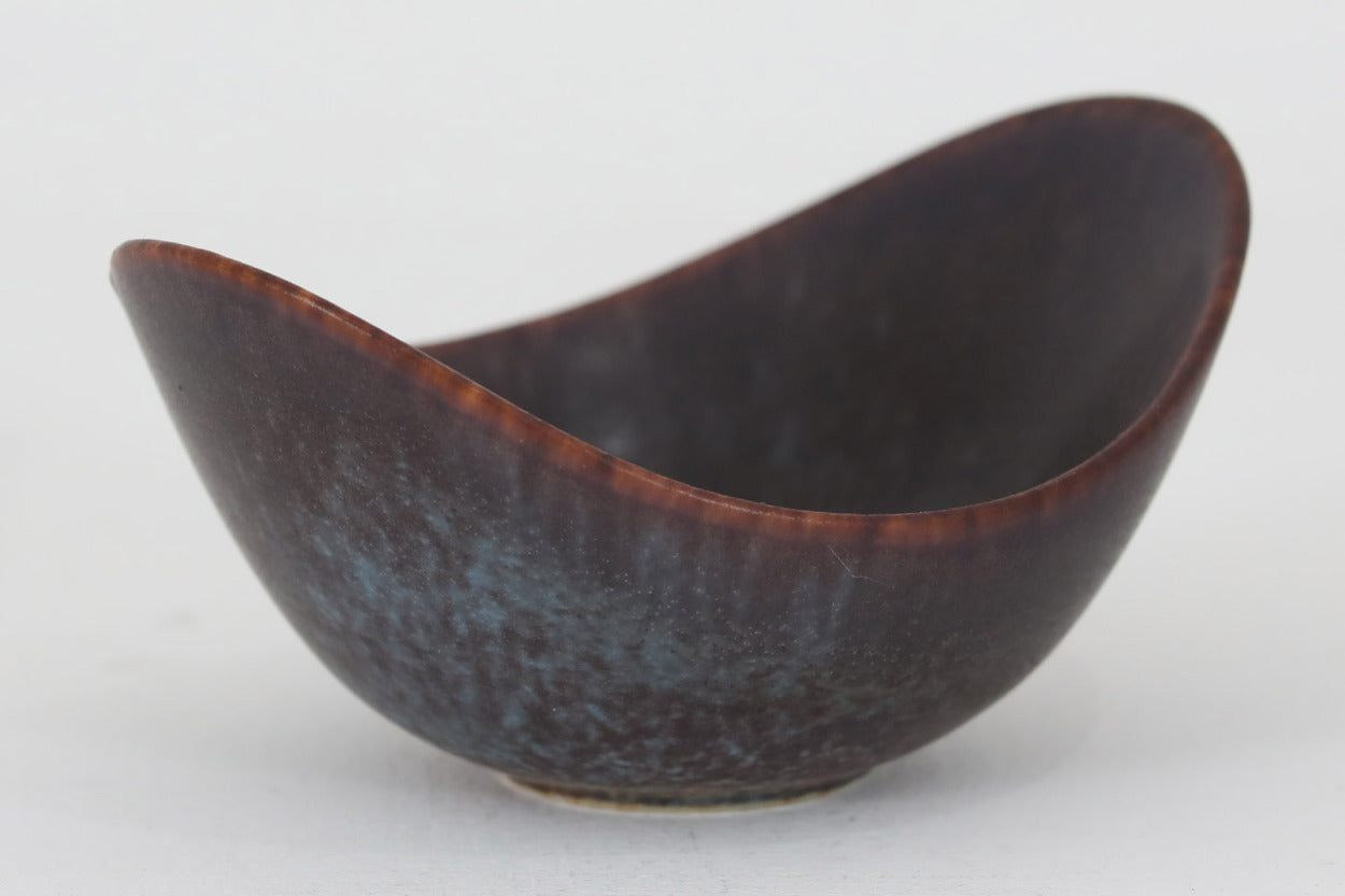 フィンランド人で彫刻家の父と、デンマーク人で陶芸家の母の元に育つGunnarNylundはデンマークで建築を学んだ後、Bing&amp;Grondahl窯、スウェーデンRorstrand窯に就業し、多くの作品を生み出しています。彼の作品は独特な流線型と釉薬が特徴で世界中で重宝されています。AROボウルは彼の最も代表的な作品で、その緩やかな美しいカーブが特徴です。また、さまざまな表情をみせる釉薬がコレクターにも人気がある理由です。