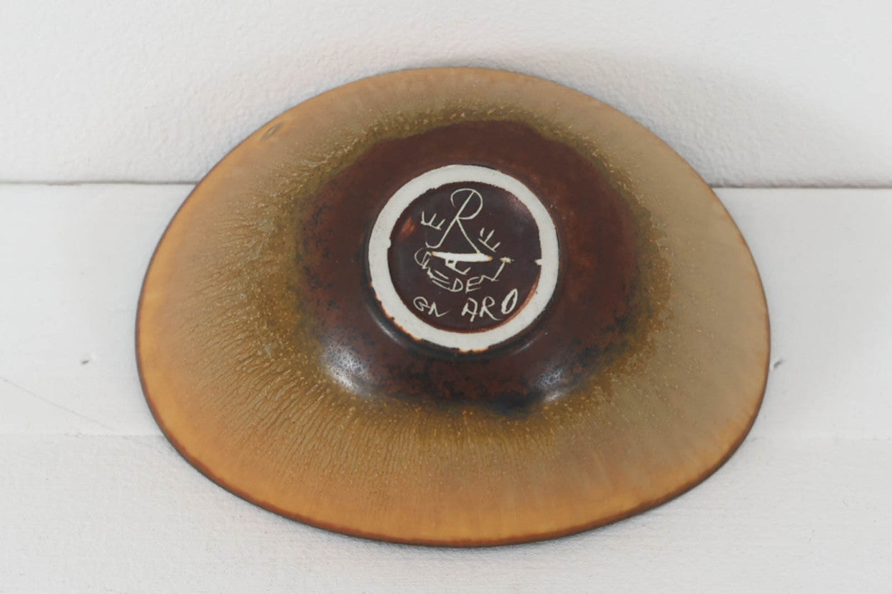 フィンランド人で彫刻家の父と、デンマーク人で陶芸家の母の元に育つGunnarNylundはデンマークで建築を学んだ後、Bing&amp;amp;Grondahl窯、スウェーデンRorstrand窯に就業し、多くの作品を生み出しています。彼の作品は独特な流線型と釉薬が特徴で世界中で重宝されています。AROボウルは彼の最も代表的な作品で、その緩やかな美しいカーブが特徴です。また、さまざまな表情をみせる釉薬がコレクターにも人気がある理由です。